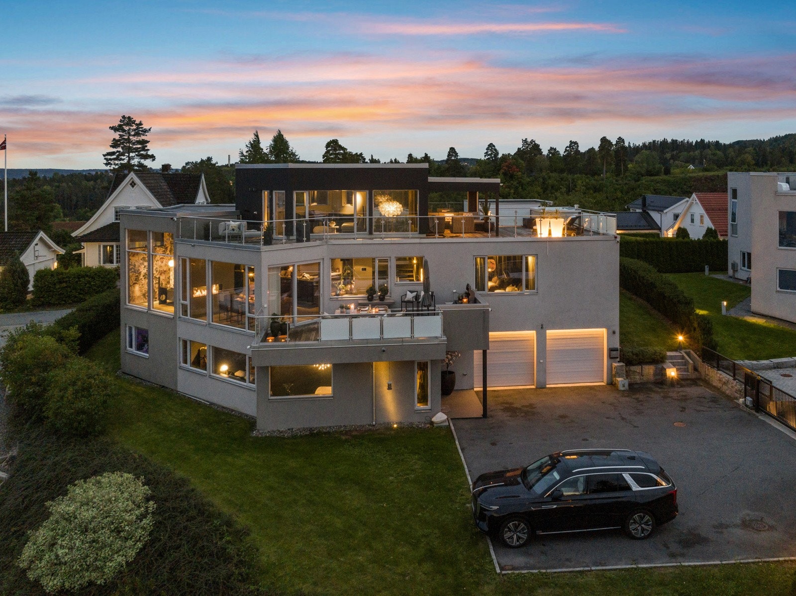 Lyssettingen gir et lekkert uttrykk når mørket senker seg. Det er parkering for to biler i dobbelgarasjen. Det er lader for elbil både i garasjen og på veggen utenfor. Galleribilde