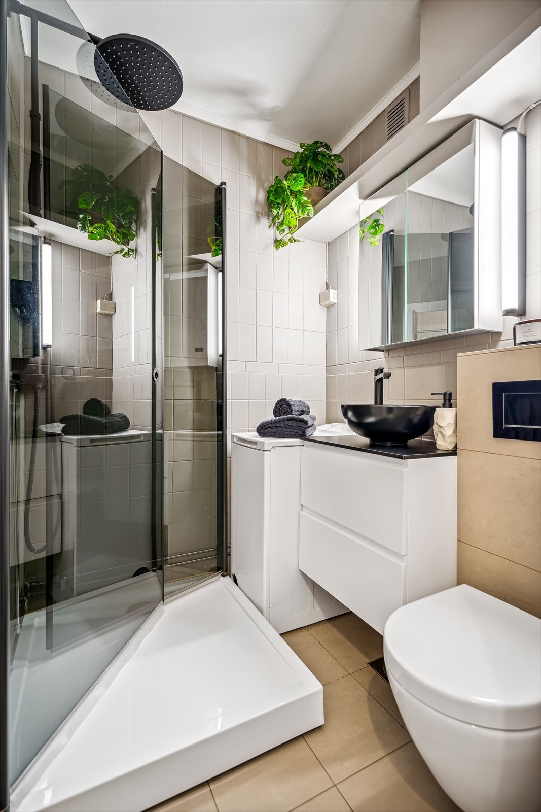 Flislagt baderom med veggmonterte dusjvegger, dusjkar, veggmontert klosett, servant med skuffer, speilskap med belysning og opplegg for vaskemaskin. Galleribilde