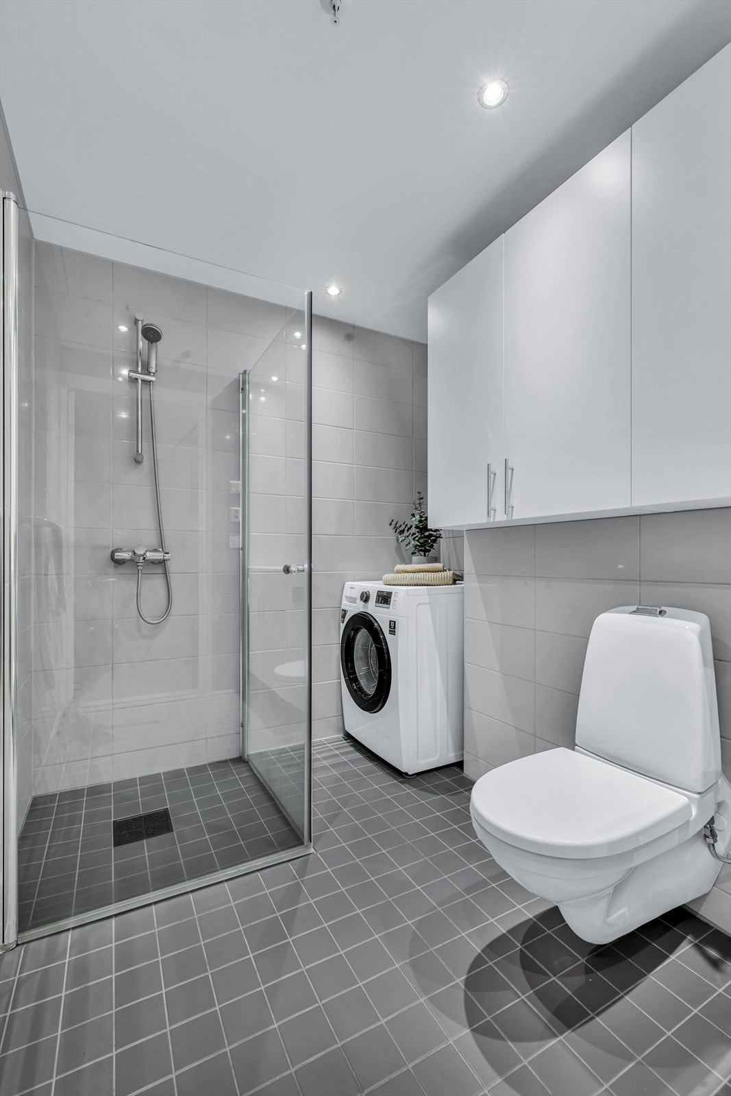 Badet er innredet med vegghengt klosett, servant innfelt i innredning, innfelt speil og dusjhjørne med svingbare glassdører. Galleribilde