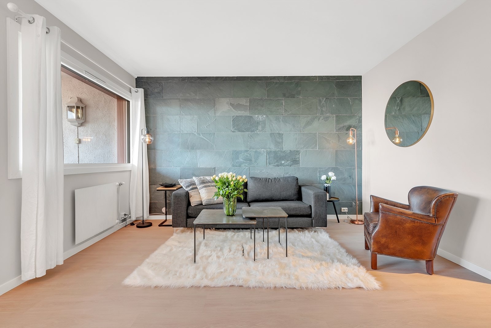 Romslig stue med laminat på gulv, malte slette vegger og en vegg med fliser samt malt tak. Her er det god plass for både sofagruppe og spisegruppe. Galleribilde