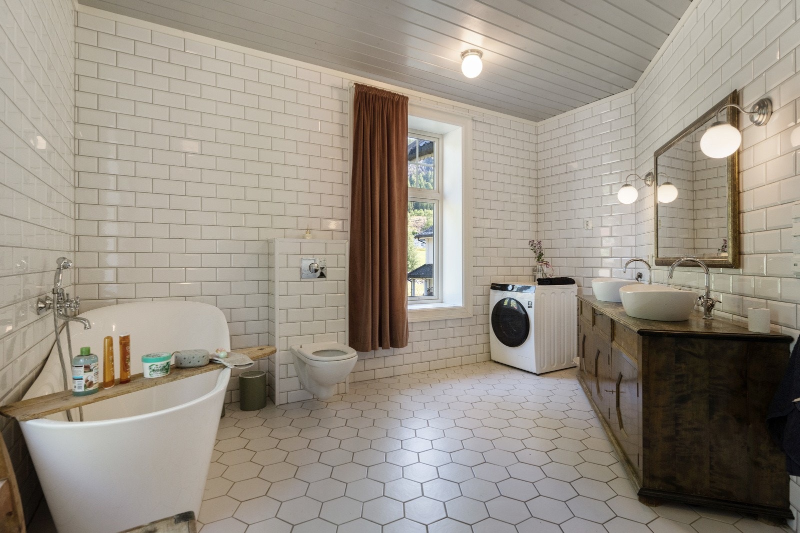 Badet er innredet med servant med skap, dusjsone med glassfelt, badekar og veggmontert WC Galleribilde