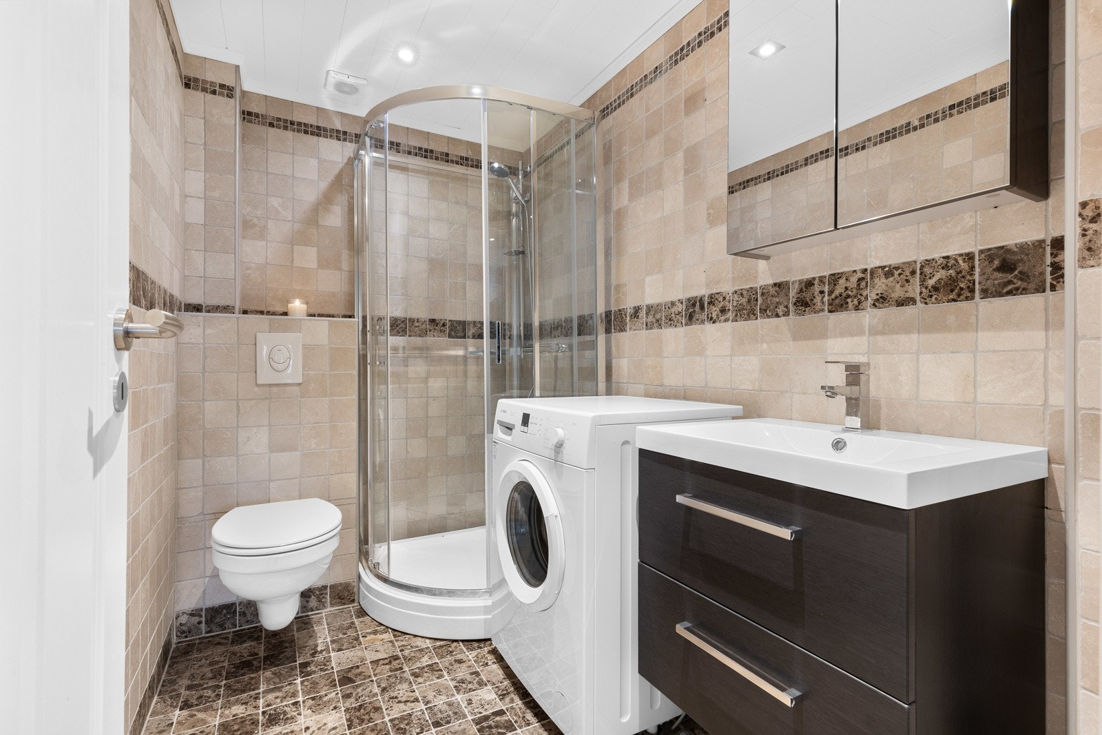 Leiligheten har et pent bad med fliser i naturtoner på vegger og gulv. Galleribilde