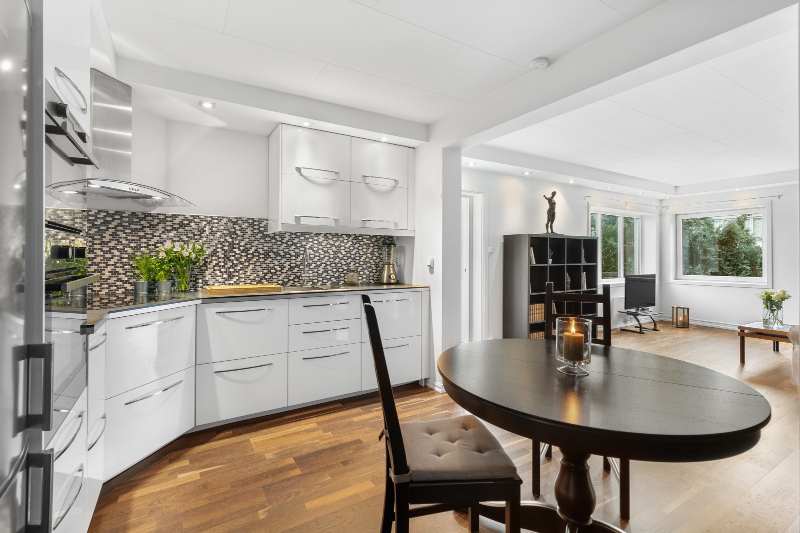 Kjøkkenet har hvit høyglansinnredning i hjørneløsning og god plass til spisebord foran en dekorativ vegg kledd med skiferfliser. Galleribilde