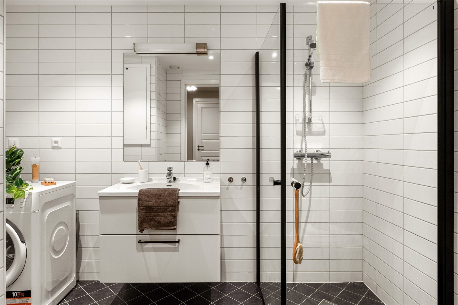 Badet er innredet med vegghengt toalett, opplegg for vaskemaskin, dusj med hengslede glassdører og baderomsinnredning med heldekkende servant, speil og belysning. Galleribilde
