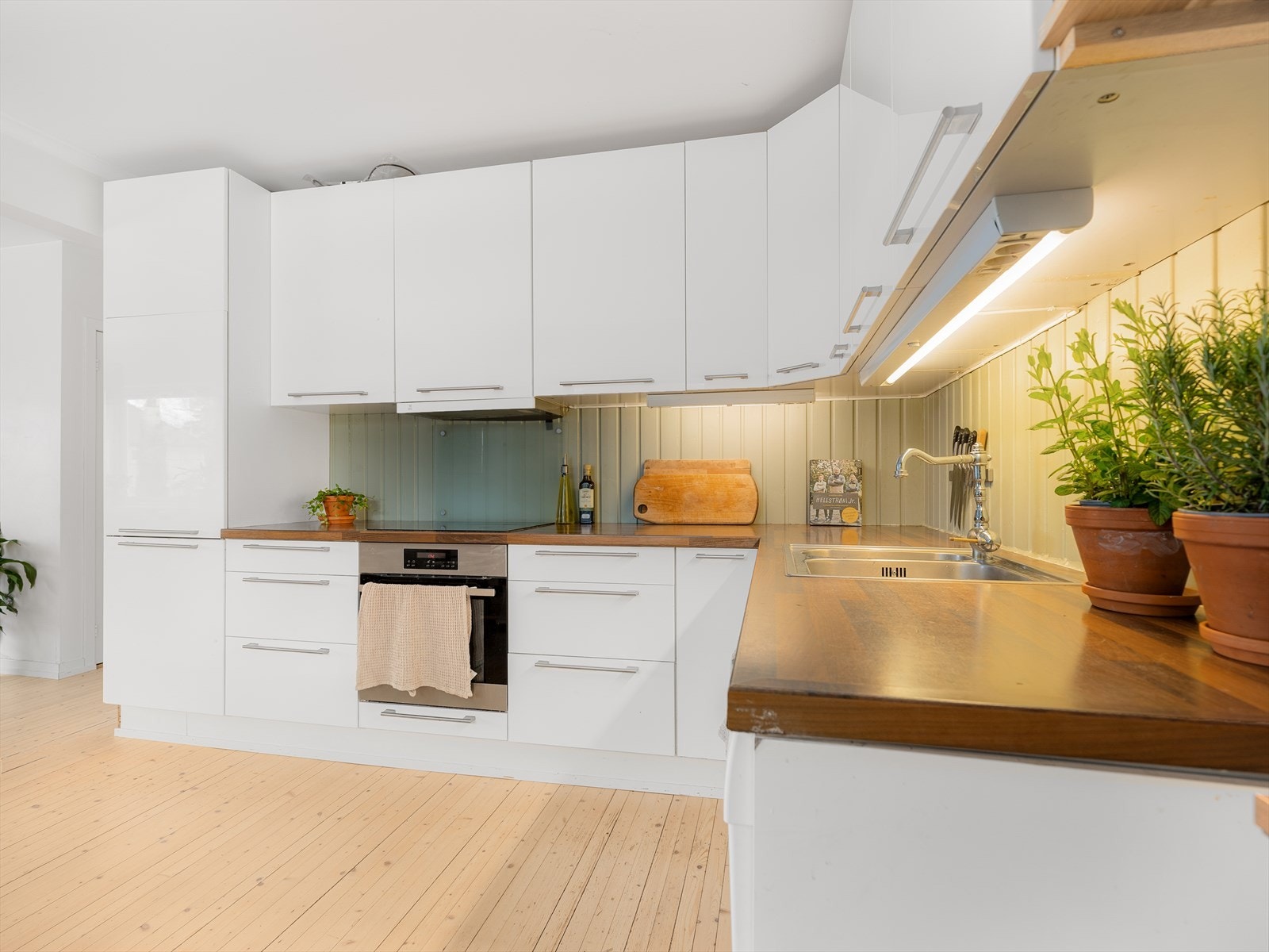 Lyse, glatte, folierte, høyglans fronter fra IKEA med laminat benkeplate og nedfelt rustfri oppvaskkum samt
ettgreps kjøkkenbatteri. Integrert komfyr med induksjons platetopp og kjøl/frys. Frittstående oppvaskmaskin. Galleribilde