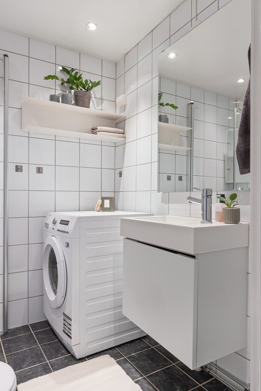 Flislagt baderom med downlights i himling. Badet er utstyrt med wc, servant med underskap og dusjhjørne med svingbare glassdører. Opplegg for vaskemaskin. Naturlig avtrekk. Galleribilde