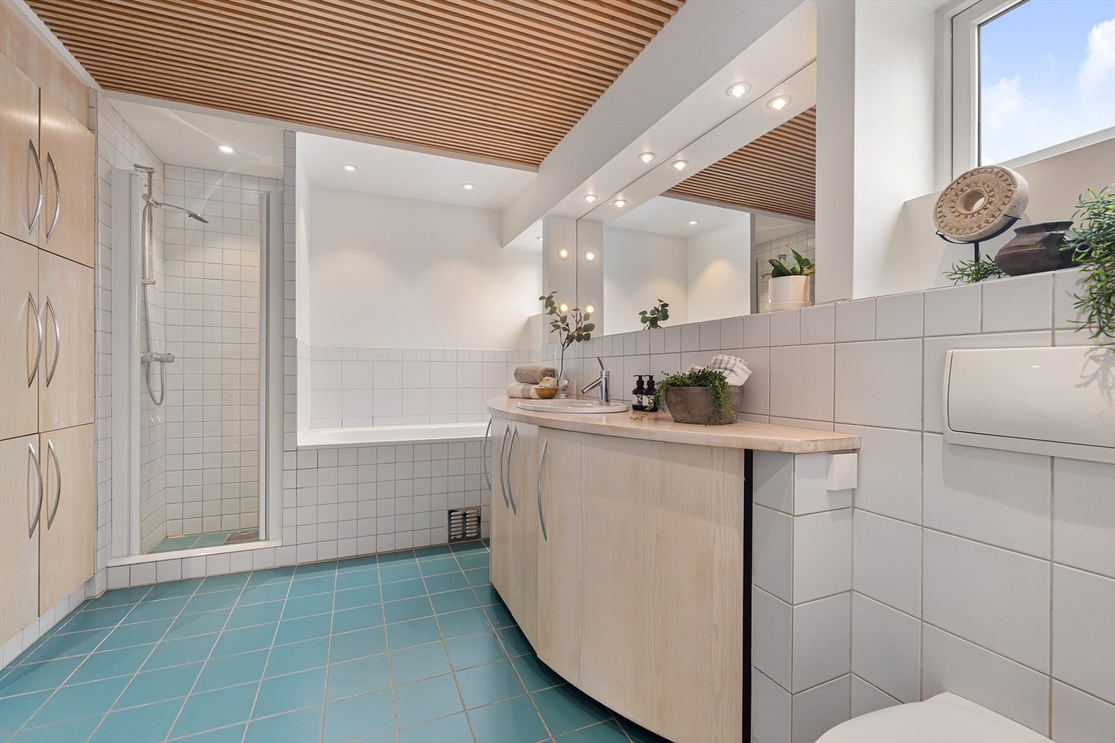 Badet er innredet med veggmontert wc, dusjnisje, boblebadekar, håndkletørker, bidet, servant i innredning med glatte fronter og speil med lys i rommet. Galleribilde