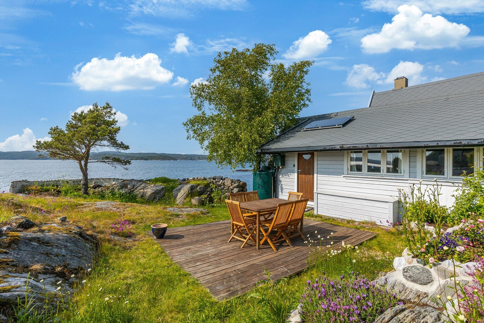 Den originale hytta fra 1956 er gråmalt med hvite karmer og med grå shingel på taket glir den fint inn i landskapet. Galleribilde