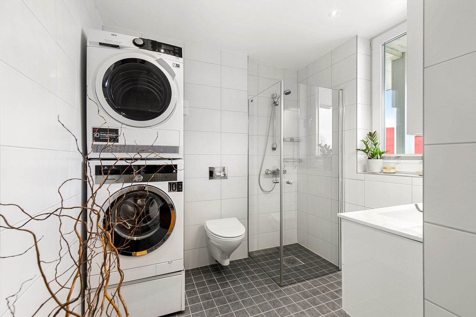 Badet har innredning med nedfelt servant, veggmontert toalett, dusjvegger/hjørne og opplegg for vaskemaskin. Galleribilde