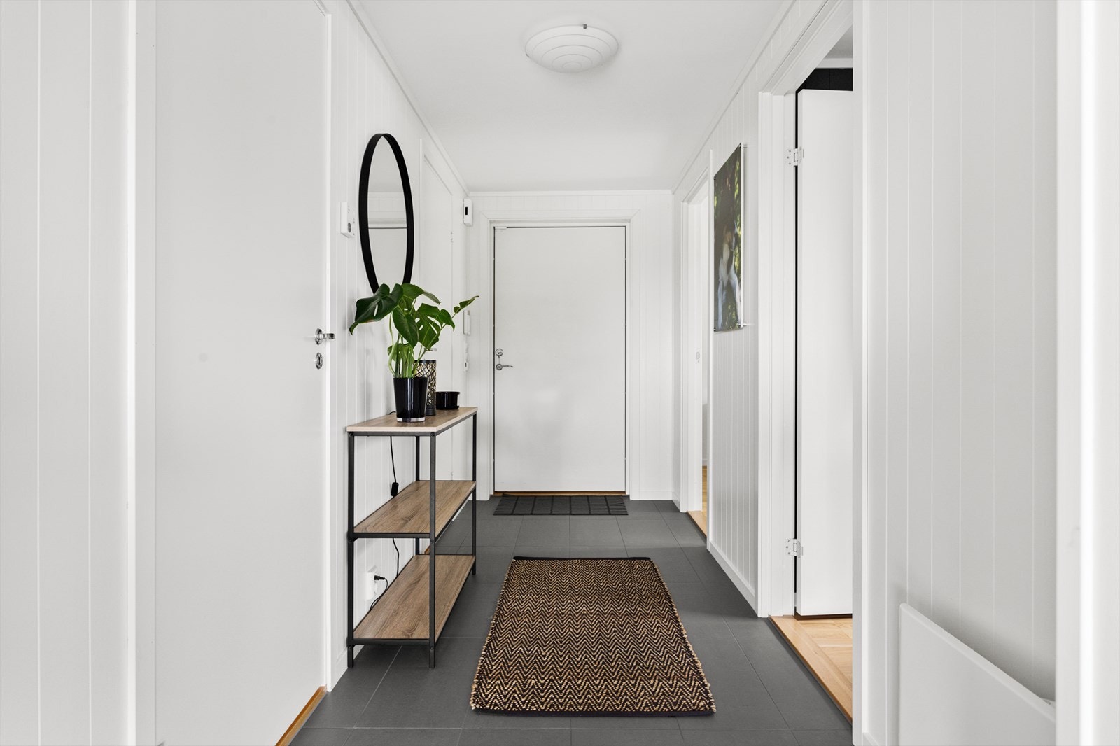 Entréen har grå gulvfliser med gulvvarme og hvitmalte panelplater på veggene. Galleribilde