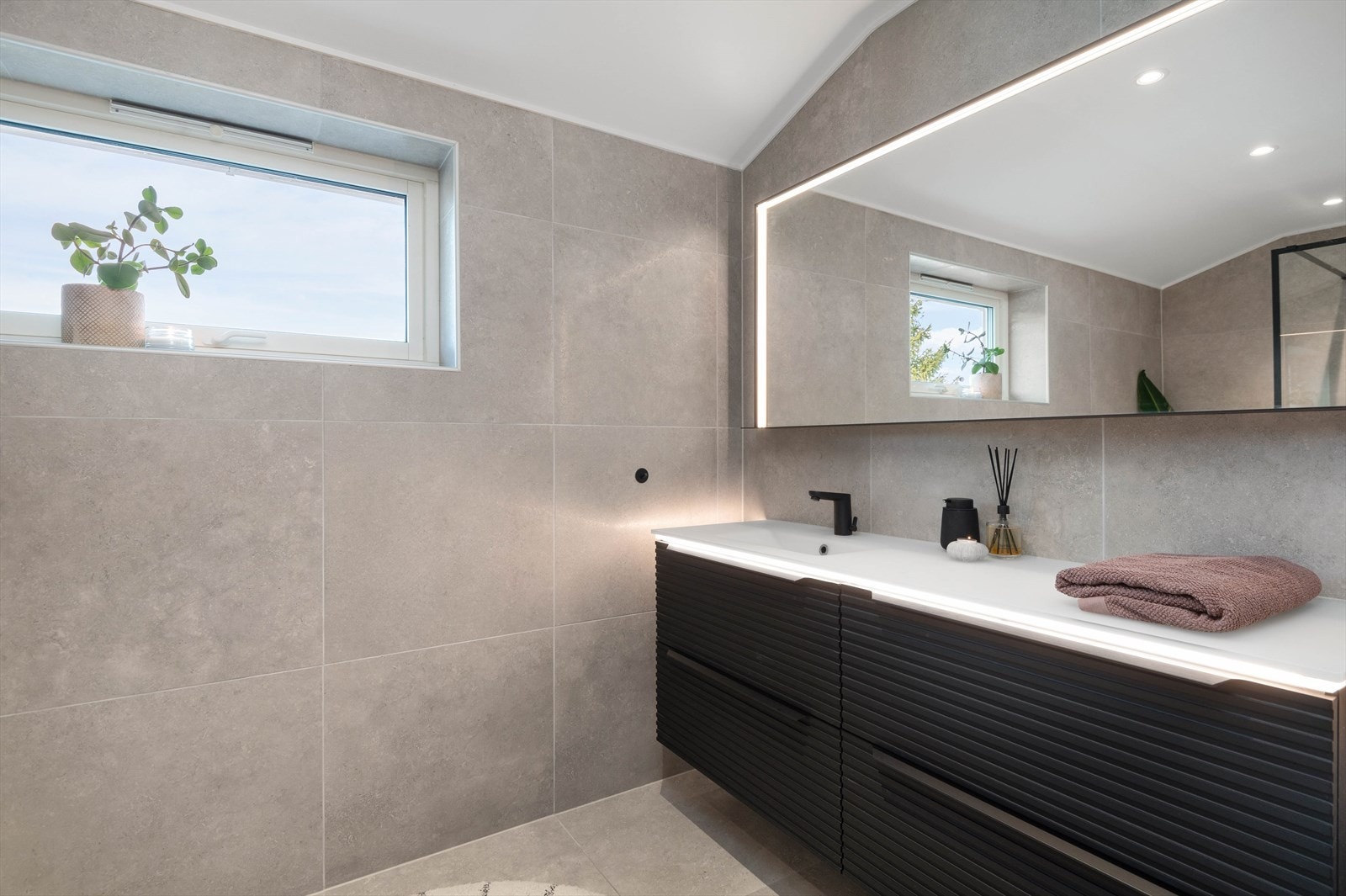 Den stilige baderomsinnredningen har servant av glass, skuffer med profilerte fronter og stort speil. Galleribilde