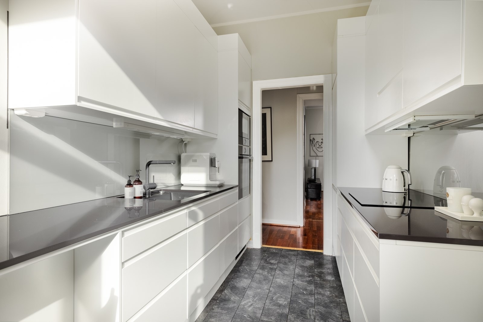 Kjøkkeninnredningen har glatte fronter i moderne utførelse, underlimt kum og benkeplate i steinkompositt. Galleribilde