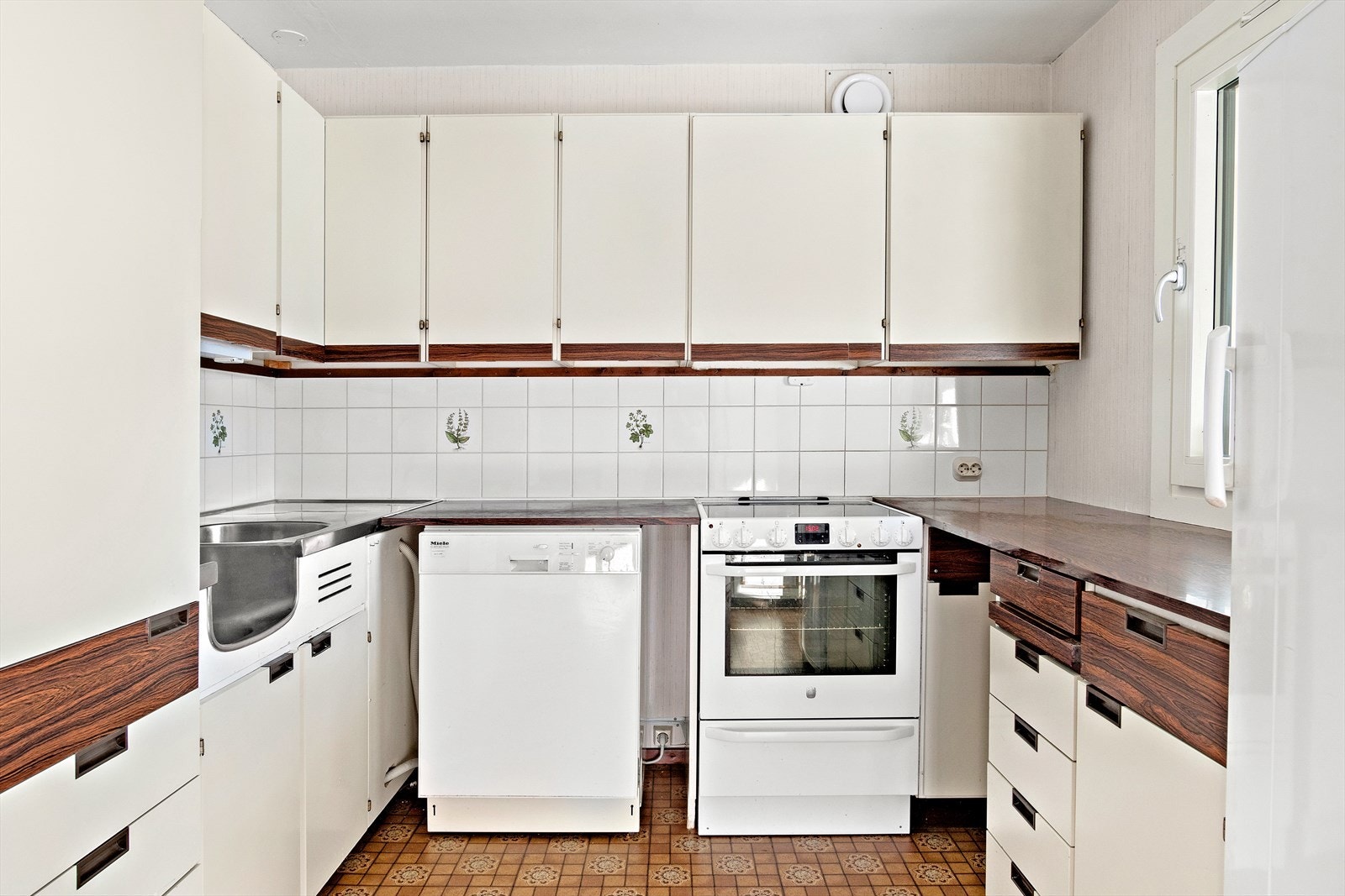 Eldre plan kjøkkeninnredning med laminert benkeplate og benkebeslag. Opplegg for oppvaskmaskin. Det er installert komfyrvakt. Det er naturlig avtrekk fra kjøkken Galleribilde