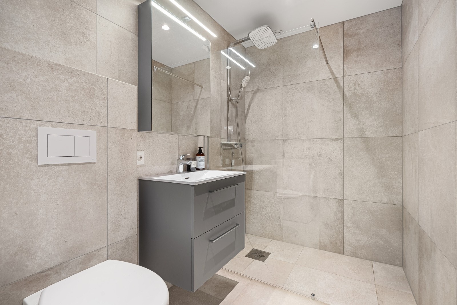 Lekkert flislagt bad med dusjnisje, vegghengt toalett og servant med innredning Galleribilde