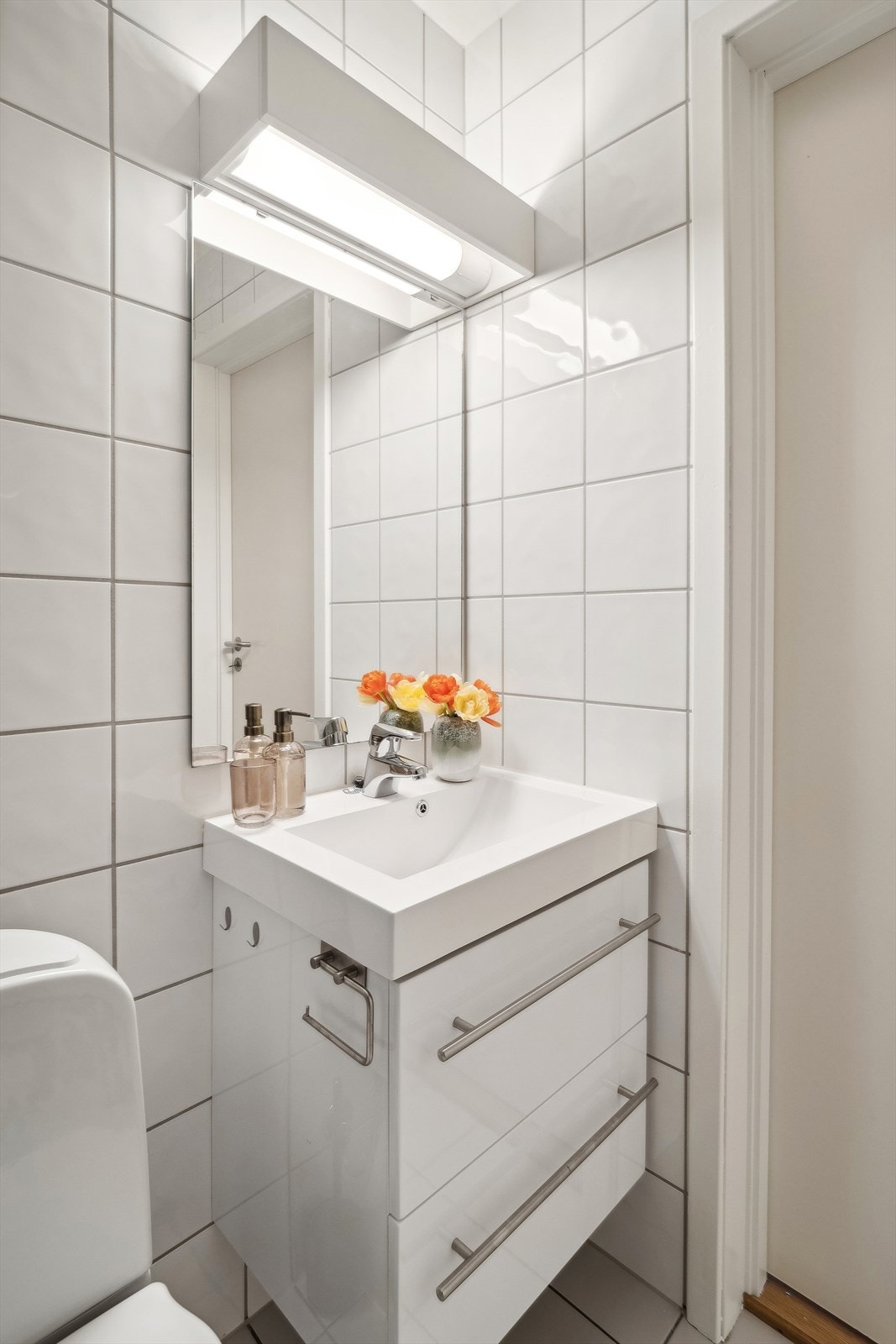 Badet har hvit innredning med nedfelt servant, gulvmontert toalett, dusjvegger/hjørne og opplegg for vaskemaskin. Galleribilde