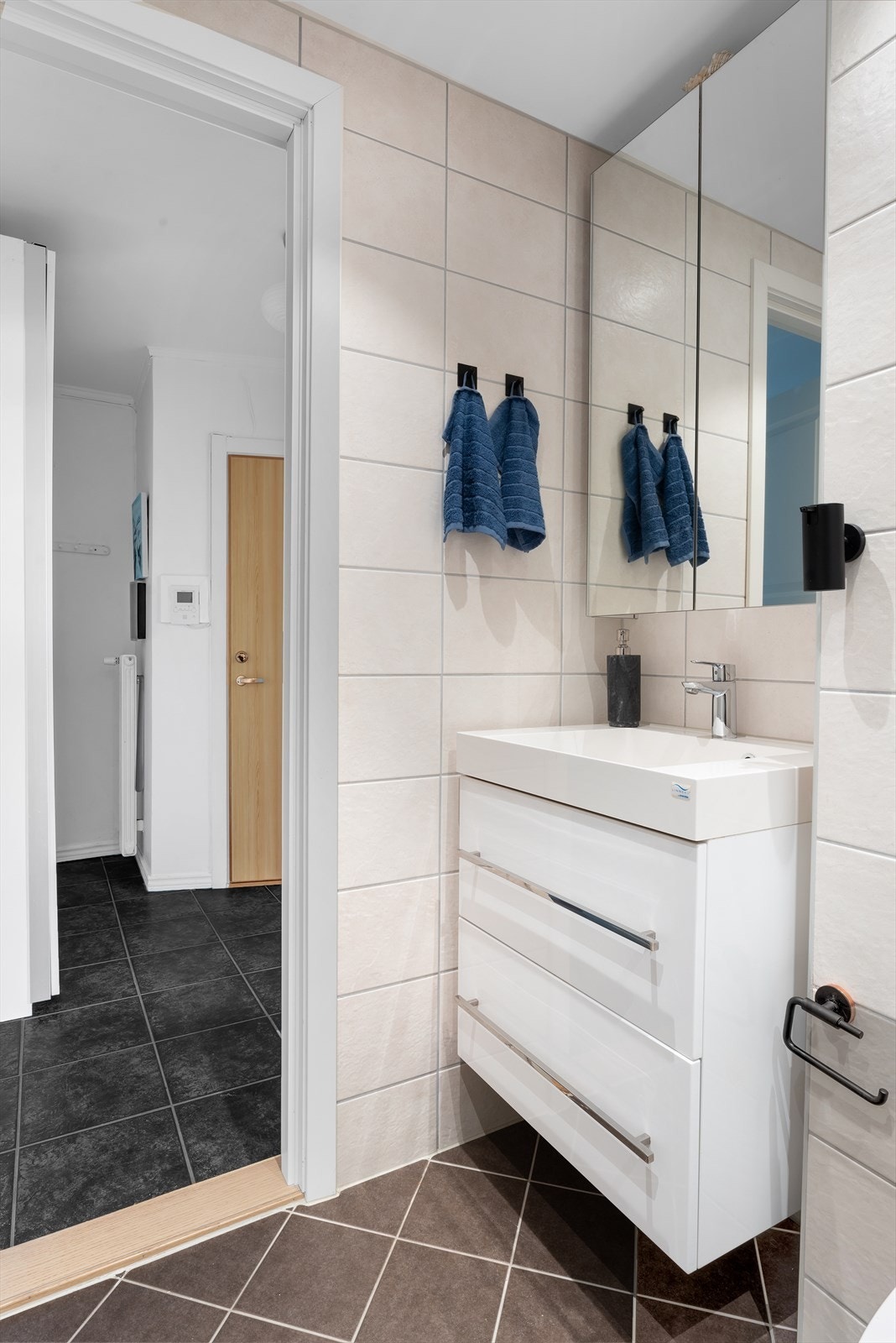 Baderomsinnredning bestående av benkeskap og veggskap med speil- og glatte fronter. Dusj med innfellbare dører i herdet glass, servant i helstøpt plate, veggfestet klosett med innebygget sisterne og opplegg for vaskemaskin. Galleribilde