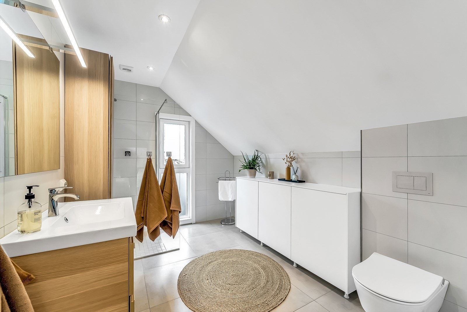 Tidløst og pent innredet bad med fliser med varmekabler på gulv og fliser på vegger. Badet er innredet med baderomsinnredning, toalett og dusjløsning med glassvegg. Galleribilde