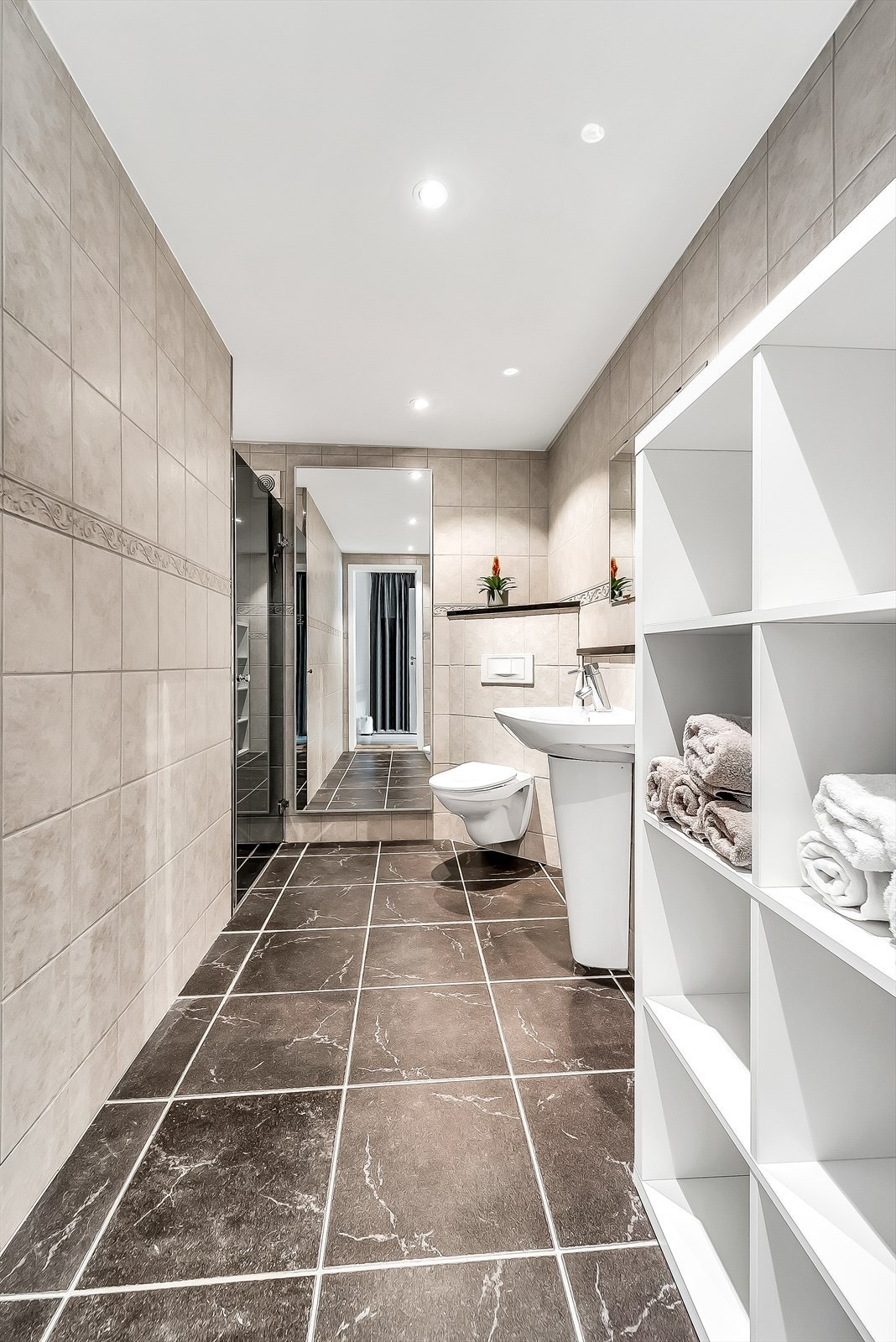 Fliselagt bad i hybeldelen med varmekabler i gulv. Innredet med dusjløsning, toalett og servant med speil. Galleribilde