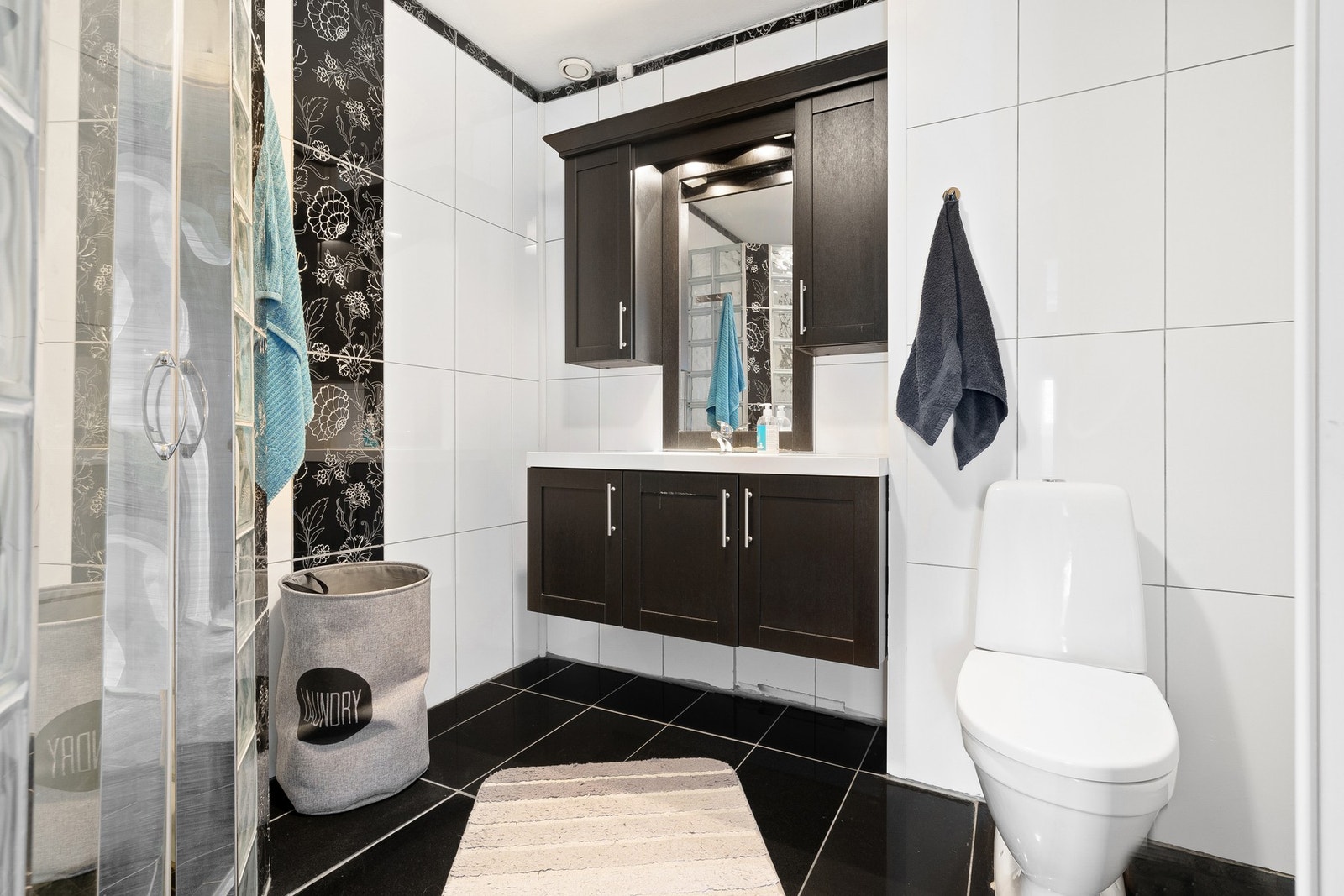 Badet har innredning med dusjhjørne, mekanisk avtrekk, gulvmontert toalett, stoppeventil og servant i skap. Galleribilde