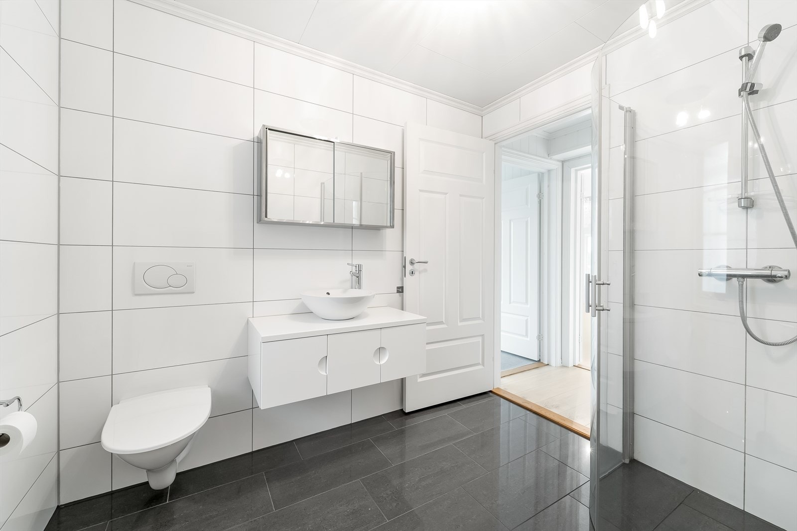 Flislagt bad med gulvvarme, innredet med baderomsinnredning, vegghengt toalett og dusjhjørne. Galleribilde