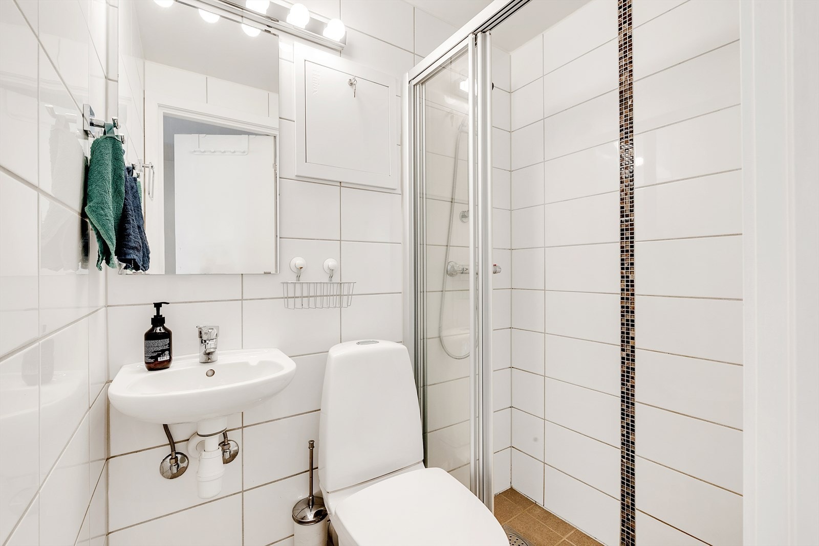 Baderomsinnredningen er bestående av veggmontert servant og veggmontert speil, med lampe. Dusjvegger på skyvbar skinne, samt veggmontert dusjstativ. Gulvmontert WC. Galleribilde