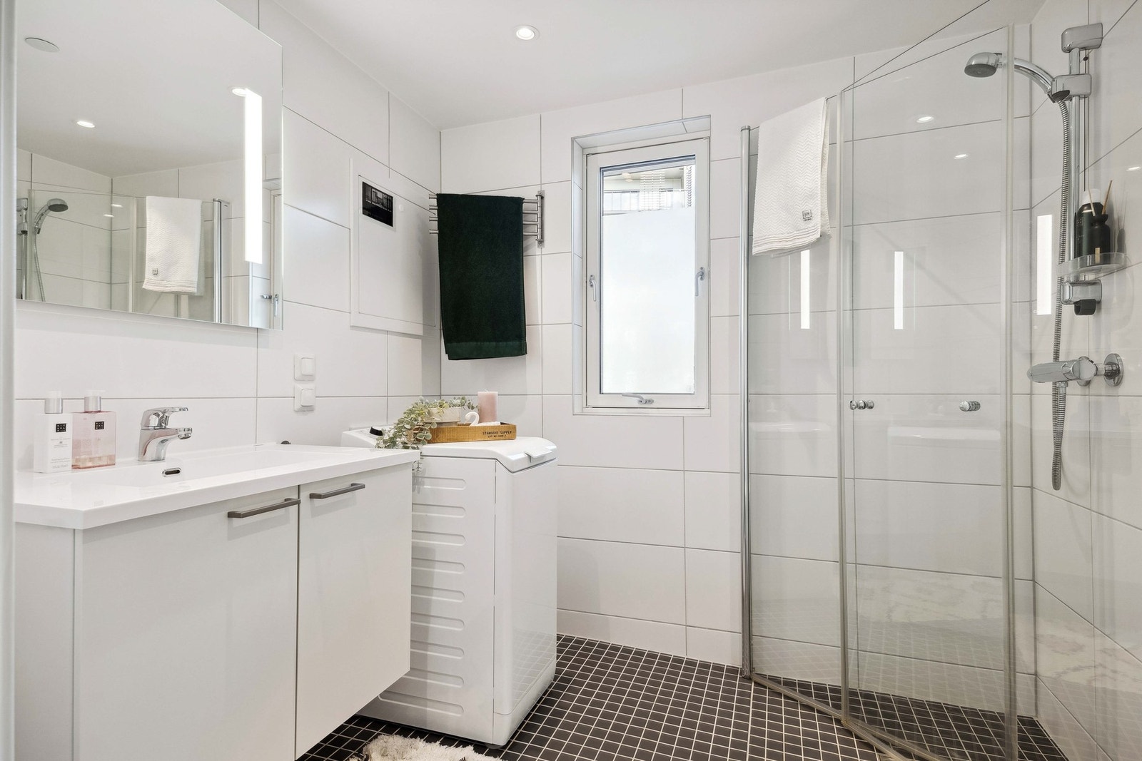 Badet fremstår innbydende og moderne. Elektriske varmekabler i baderomsgulvet, plassbesparende og innfellbare dusjdører i glass, spotter i himling, samt kran og avløp for vaskemaskin. Galleribilde