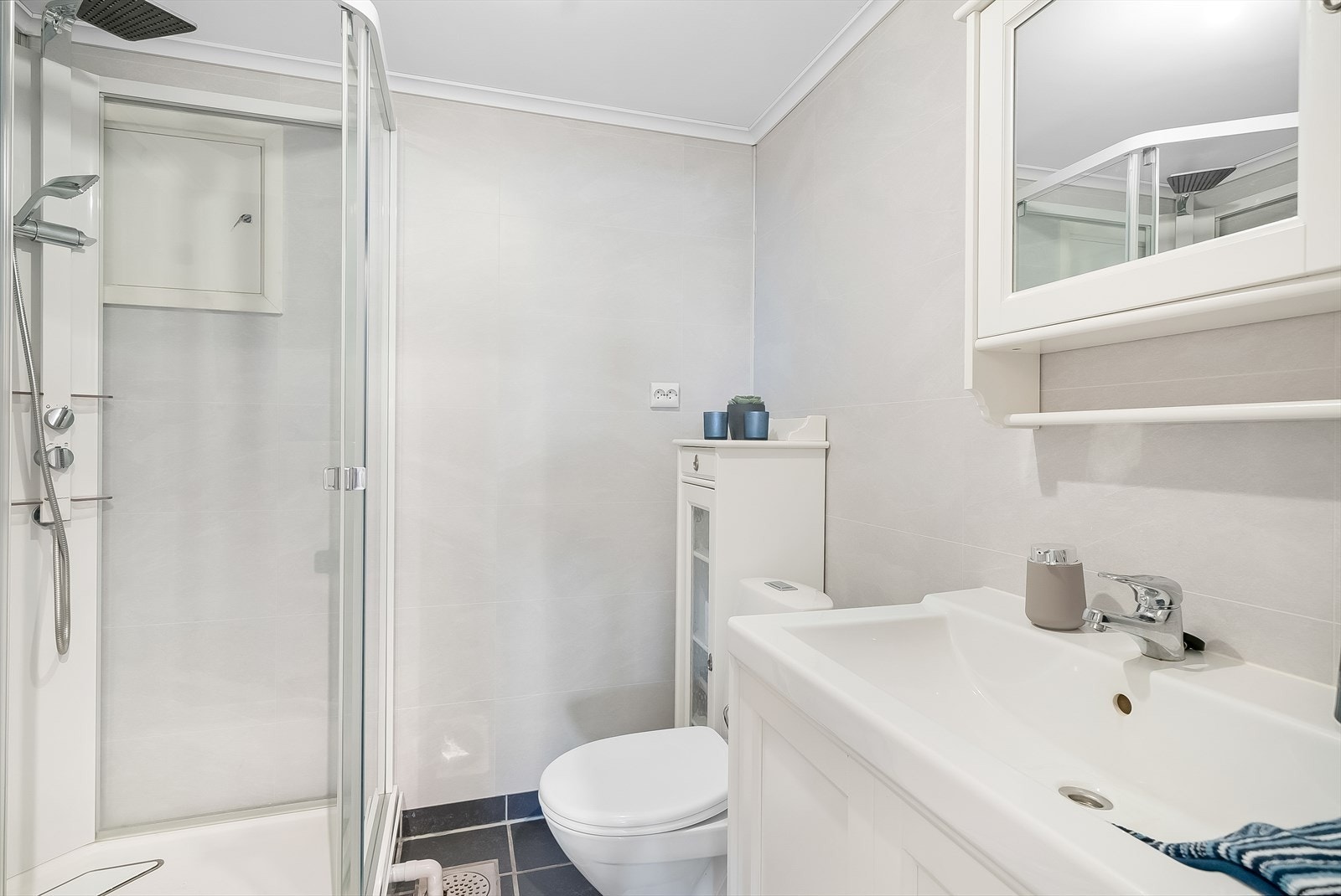 Bad i hybeldel med fliser med varmekabler på gulv og baderomsplater på vegg. Innredet med baderomsinnredning. toalett og dusjkabinett. Galleribilde