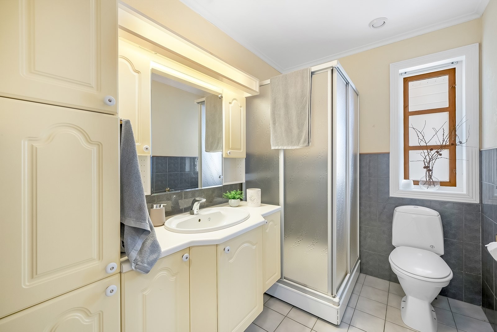 Bad i 1. etasje med fliser på gulv med varmekabler og fliser/tapet på vegg. Rommet er innredet med baderomsinnredning, toalett og dusjkabinett. Galleribilde