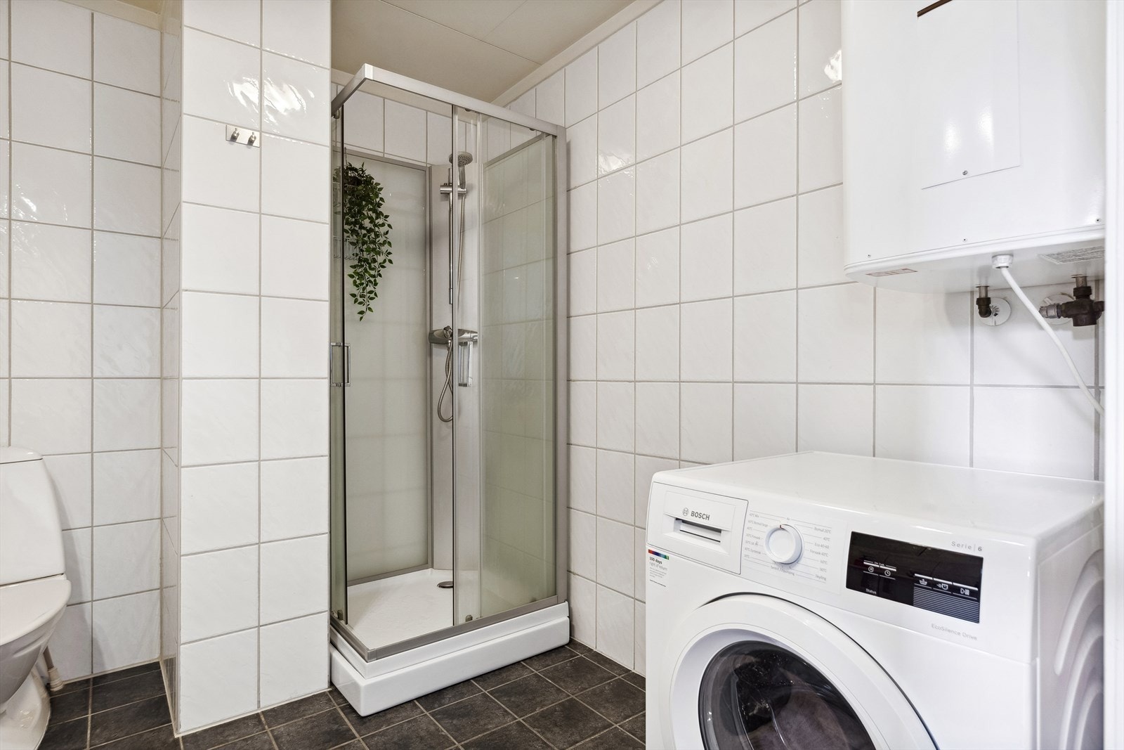 Badet har en klassisk stil med flislagte overflater, og hvit baderomsinnredning med benkeskap, servant og speilskap. Galleribilde