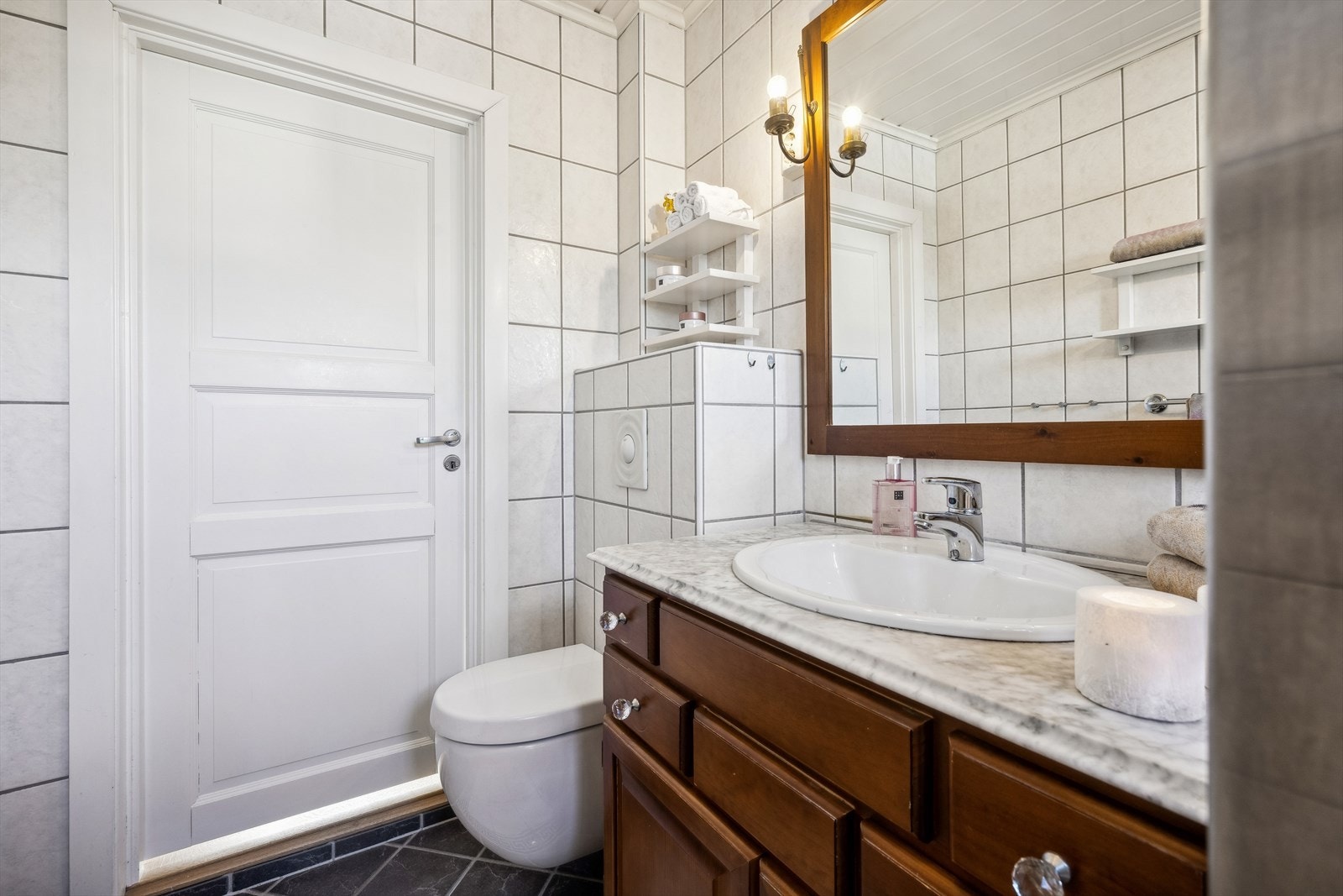 Badet er innredet med vegghengt toalett, servant med skap, speil, og dusjhjørne Galleribilde