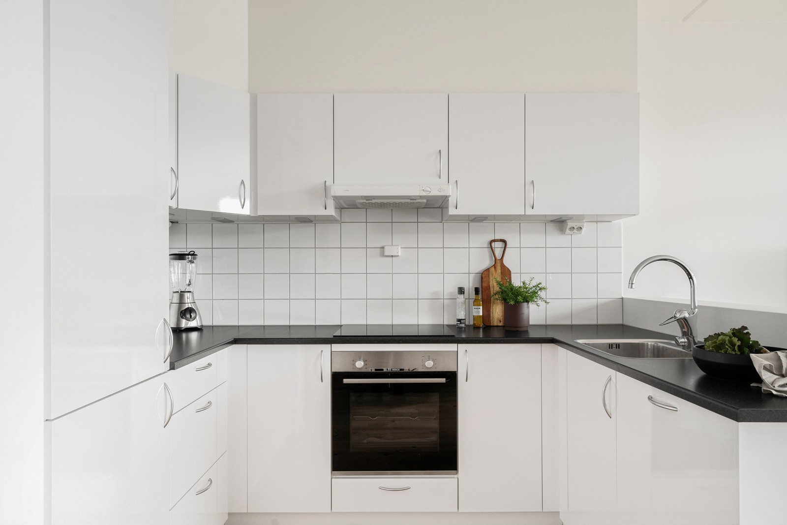 Kjøkkenhjørne med hvit innredning med over- og underskap som sikrer rikelig med oppbevaringsplass.