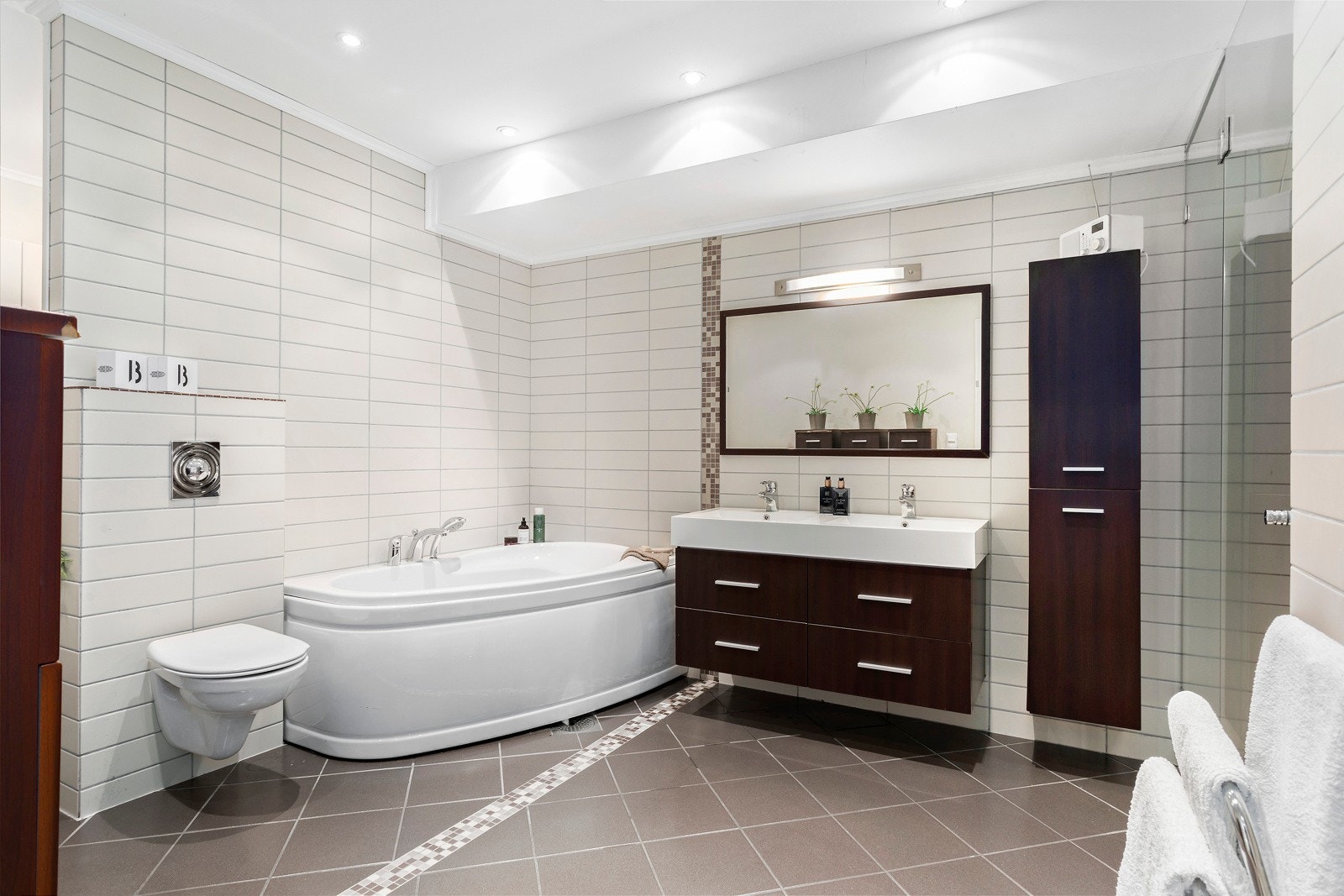 Stort flislagt bad/wc med badekar- og dusjnisje - solid innredning med dobbbelvask - downlights Galleribilde