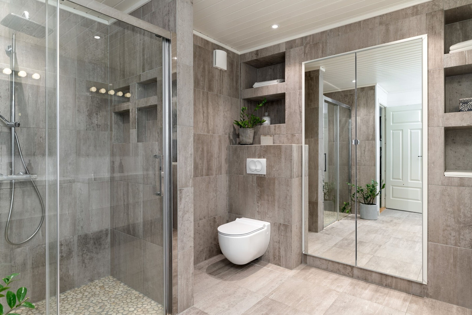 Badet har dusjhjørne, veggmontert toalett og flere integrerte hyller. Galleribilde