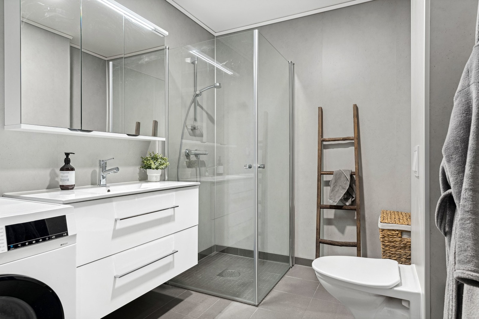 Badet er utstyrt med baderomsinnredning, dusjplass med dusjvegg, toalett og plass til både vaskemaskin og tørketrommel Galleribilde