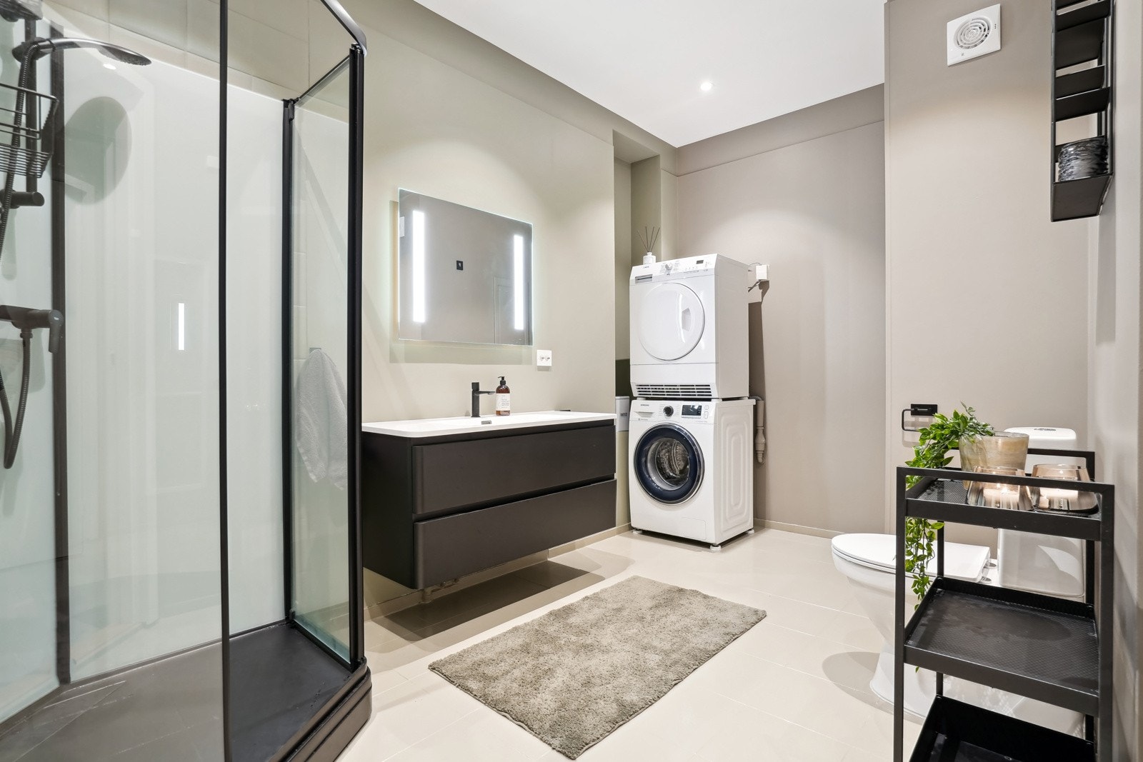 Lekkert bad med romslig servantskap, dusjkabinett, gulvmontert toalett, gulvvarme og opplegg for vaskemaskin. Galleribilde