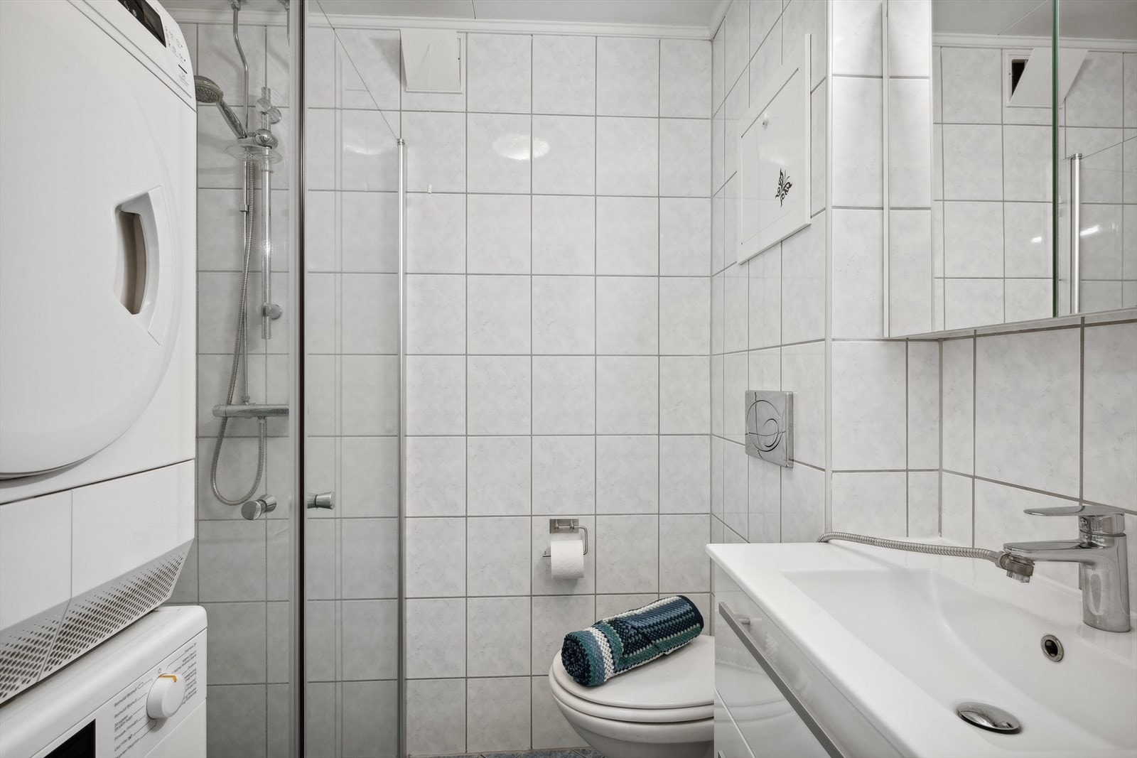 Badet har innredning med nedfelt servant, overskap med speil. veggmontert toalett, dusjvegger/hjørne og opplegg til vaskemaskin. Galleribilde