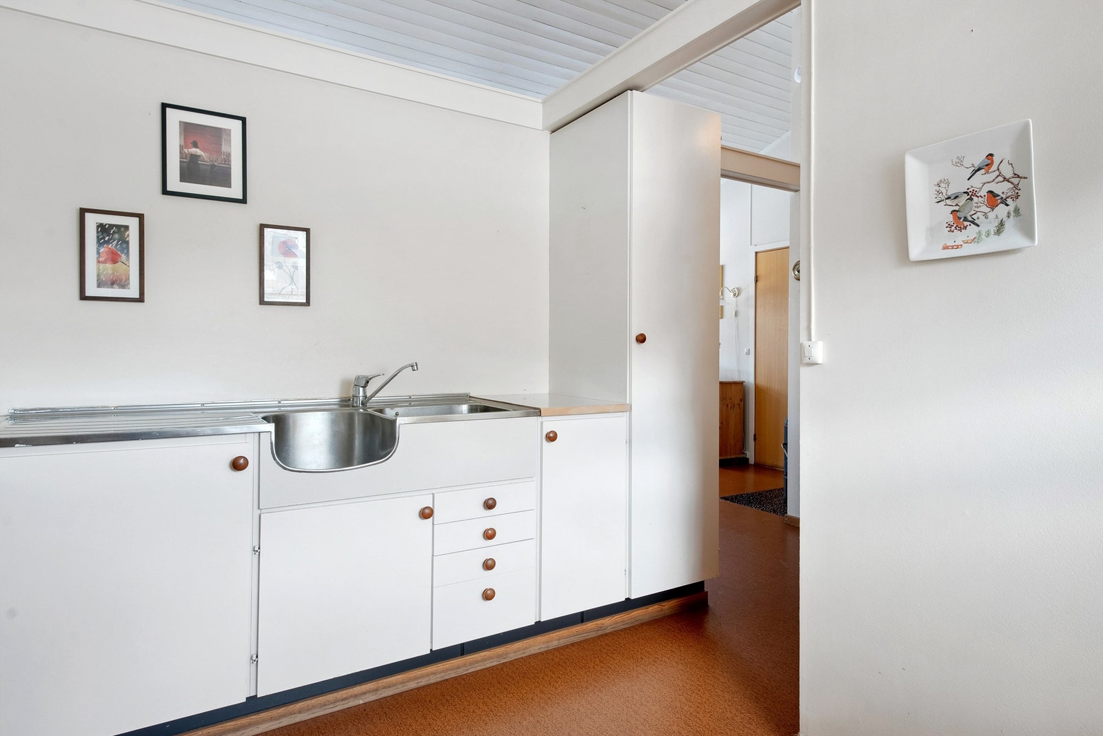Det er åpen løsning for kjøl-/fryseskap og komfyr, og montert kjøkkenventilator over komfyrplass. Kjøkkenet har god takhøyde og delvegg med åpning øverst mot stuen, dette gir rommet en luftig følelse Galleribilde