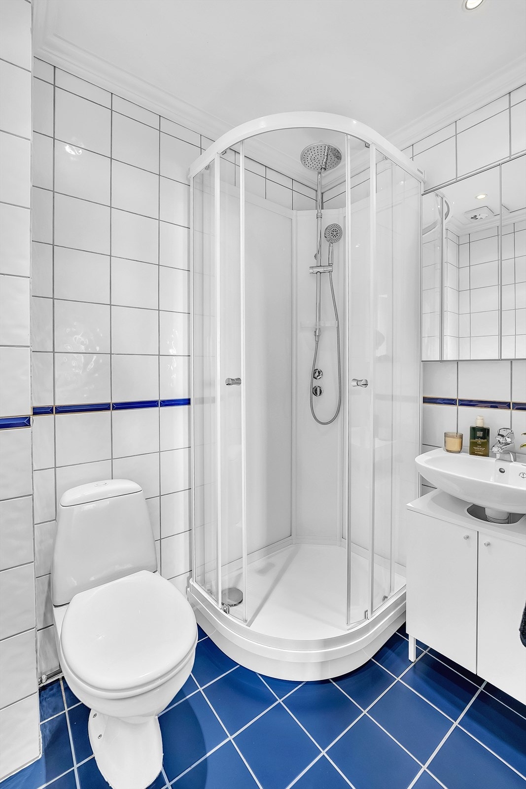 Bad med dusjkabinett, toalett og servant med skap samt vegghengt speilskap. Galleribilde