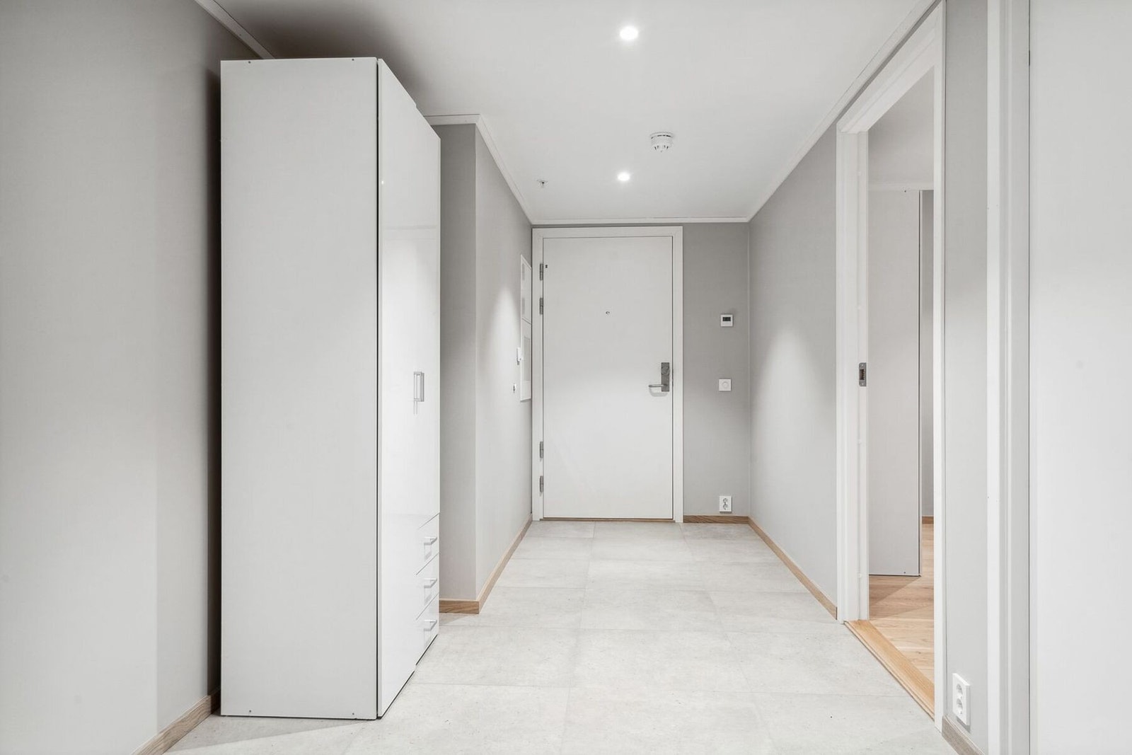 Innbydende gang som er fliselagt med store 60x60 fliser i en gråtone som harmonerer med fargen på veggen. Galleribilde