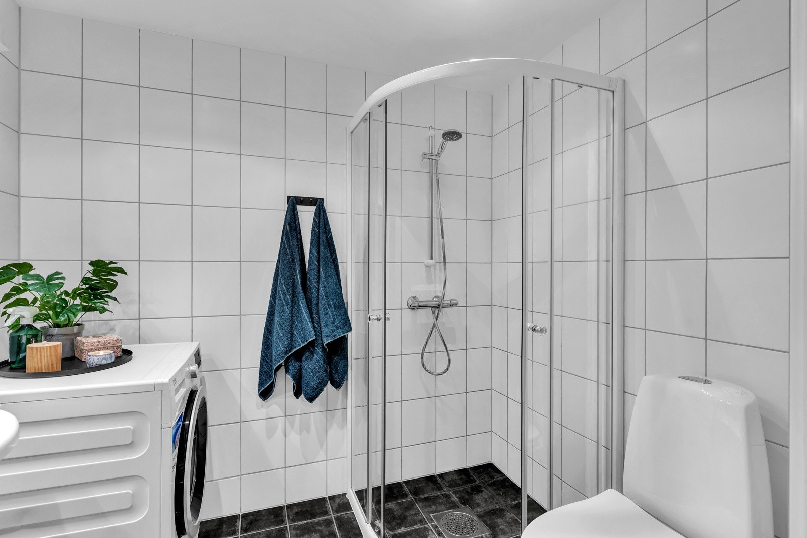 Rommet er videre utstyrt med dusjhjørne med skyvedører, heldekkende servant med skap, speil med belysning og gulvstående toalett Galleribilde