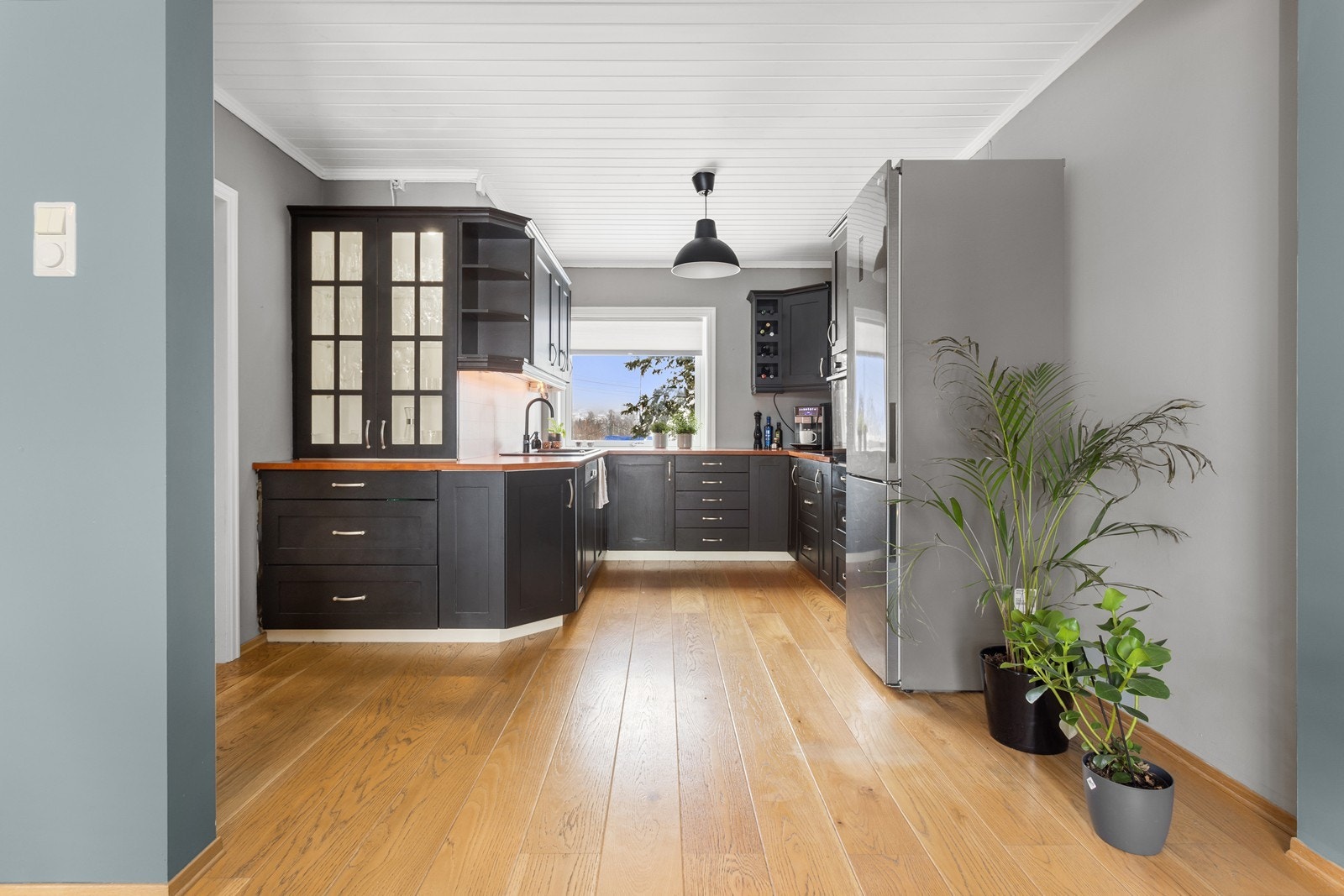 Åpen kjøkkenløsning mot spisestue. Kjøkkeninnredningen har profilerte fronter i matt sort utførelse, vitrineskap med glassfelt i dørene og integrert belysning. Galleribilde