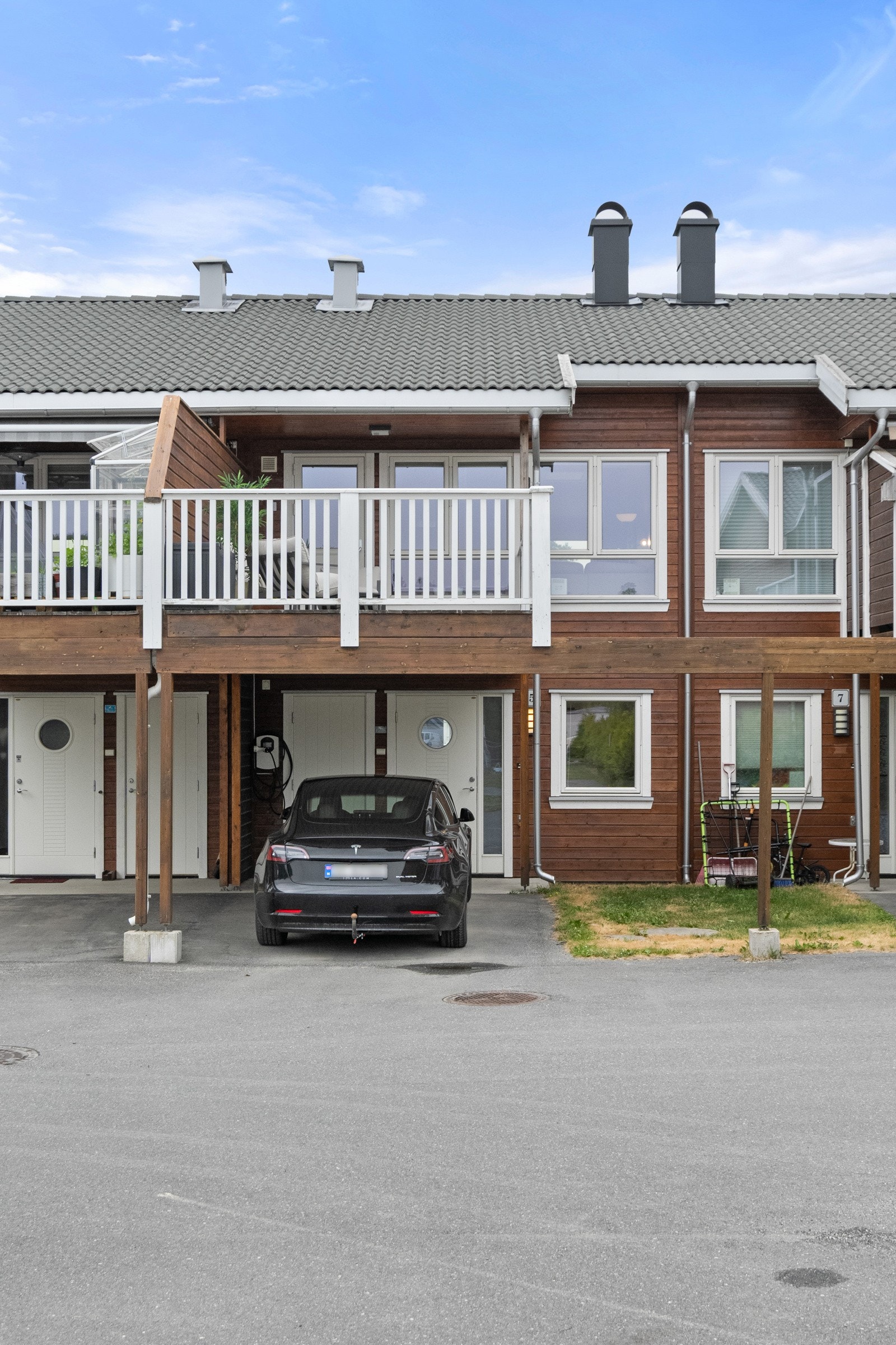 Boligen har en asfaltert carport med elbillader montert på vegg. Galleribilde