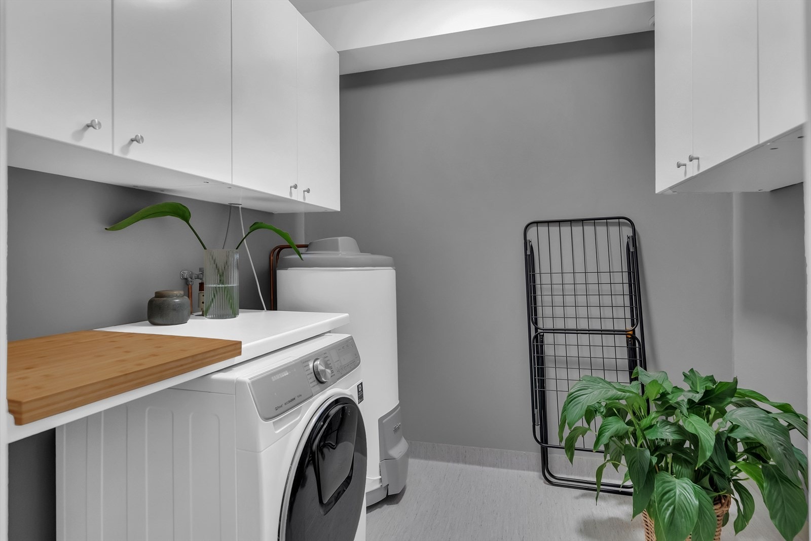 Vegg i vegg med baderommet ligger et praktisk vaskerom utstyrt med benkeskap, overskap, varmtvannsbereder og opplegg til vaskemaskin. Galleribilde