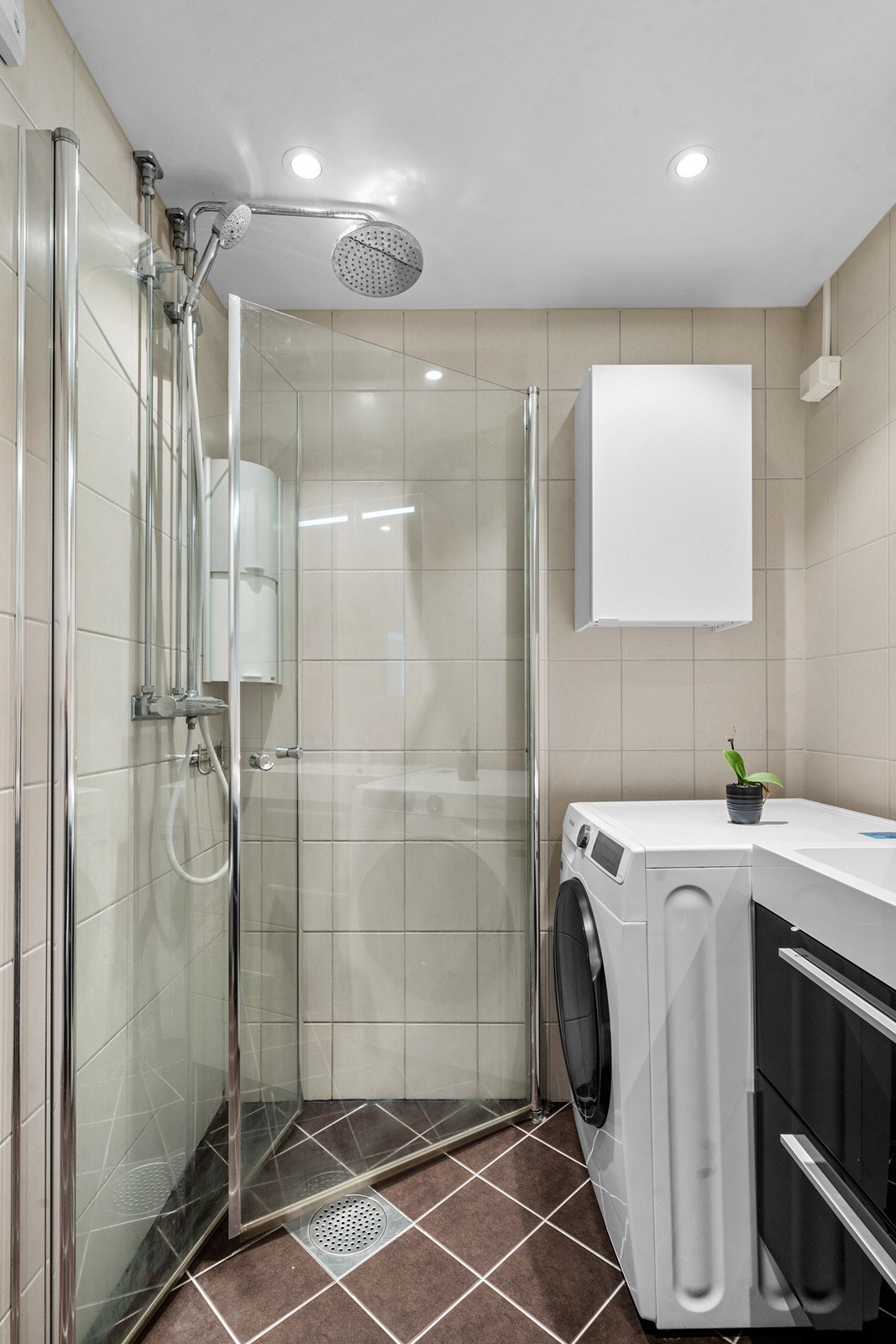 Badet er utstyrt med dusjhjørne med innfellbare glassvegger, vegghengt wc, servantinnredning med skuffer og overskap, samt opplegg og plass til vaskemaskin. Galleribilde