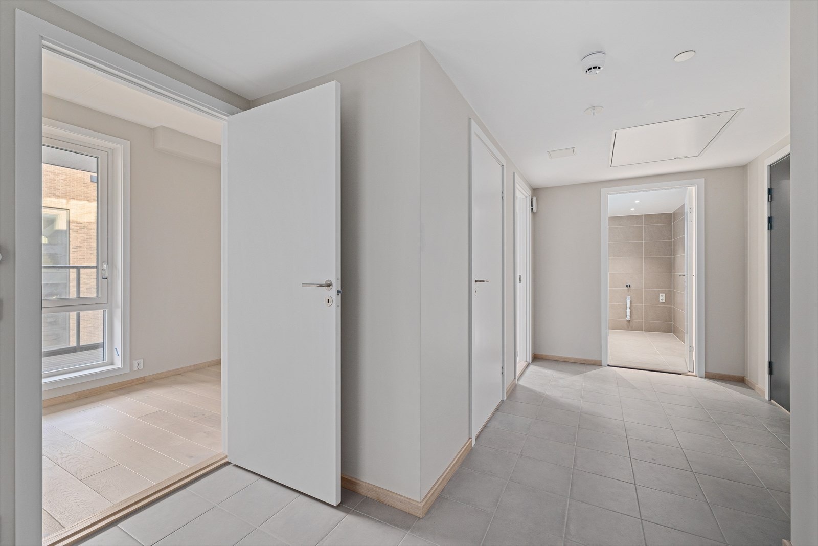 Romslig flislagt gang med 60*60 fliser på gulv. Vannbåren gulvvarme. Downlights i tak. Galleribilde