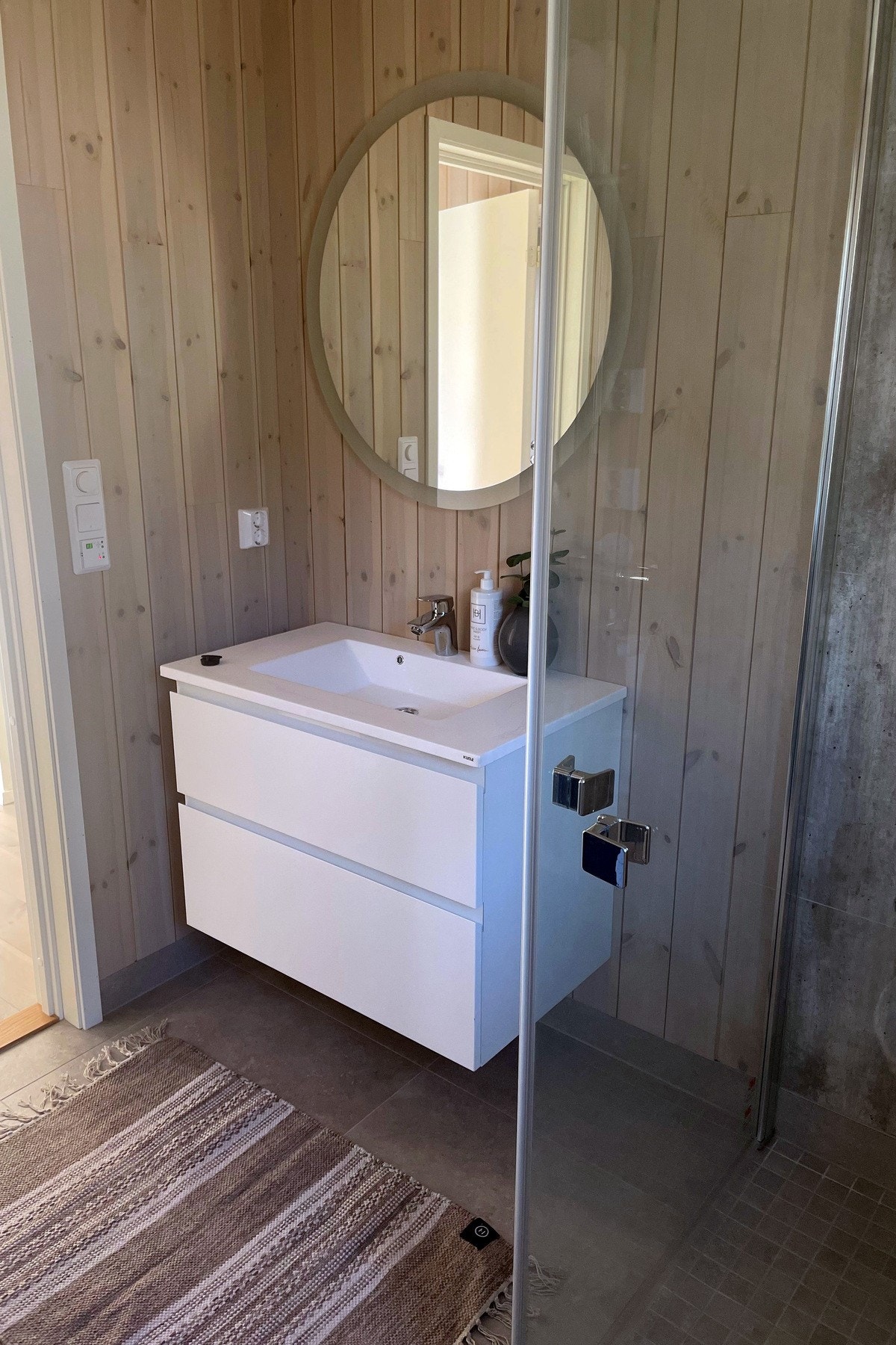 Det er flis på gulv, flislignende baderomsplater på vegger i dusjsone og ellers er det beiset panel på vegger. Galleribilde