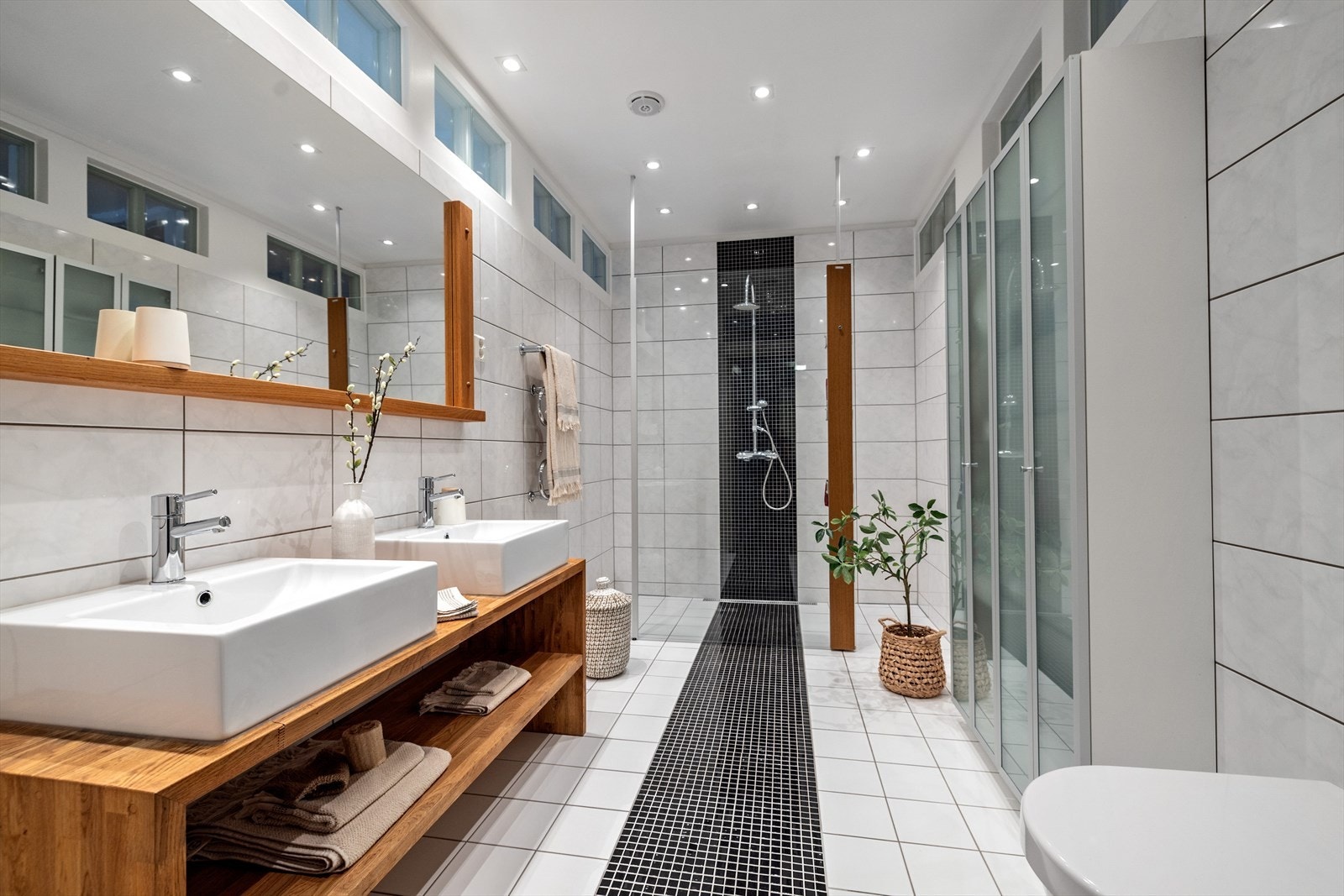 Moderne flislagt baderom med gulvvarme. Badet er innredet med to servanter med underhylle, vegghengt toalett og dusjnisje Galleribilde