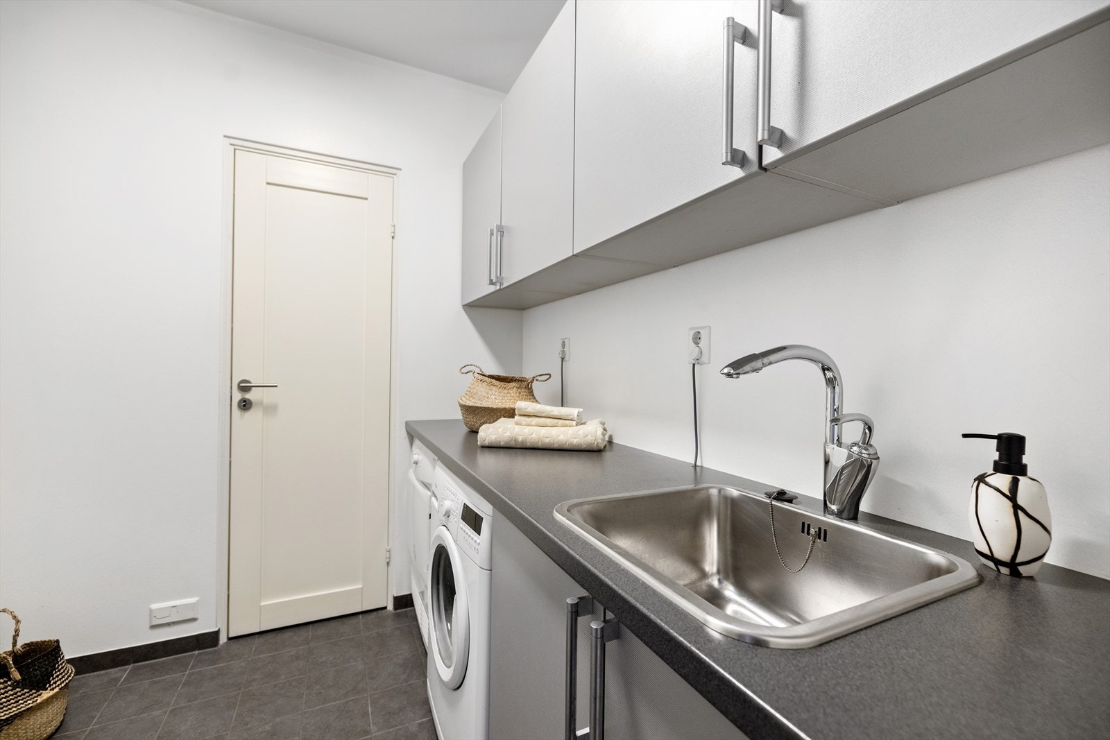 Praktisk vaskerom med gulvvarme. Det er god plass til oppbevaring av vaskemidler og annet utstyr i overskapene på vaskerommet Galleribilde