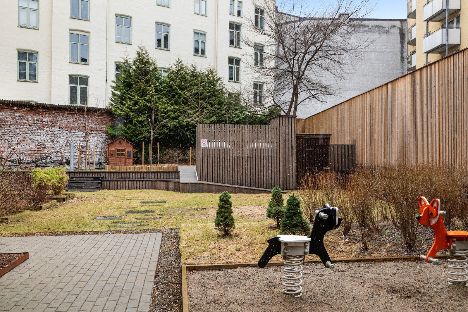 Pent opparbeidet gårdsrom med gressplen, stenbelagte internveier og lekeapprater for de minste. Galleribilde