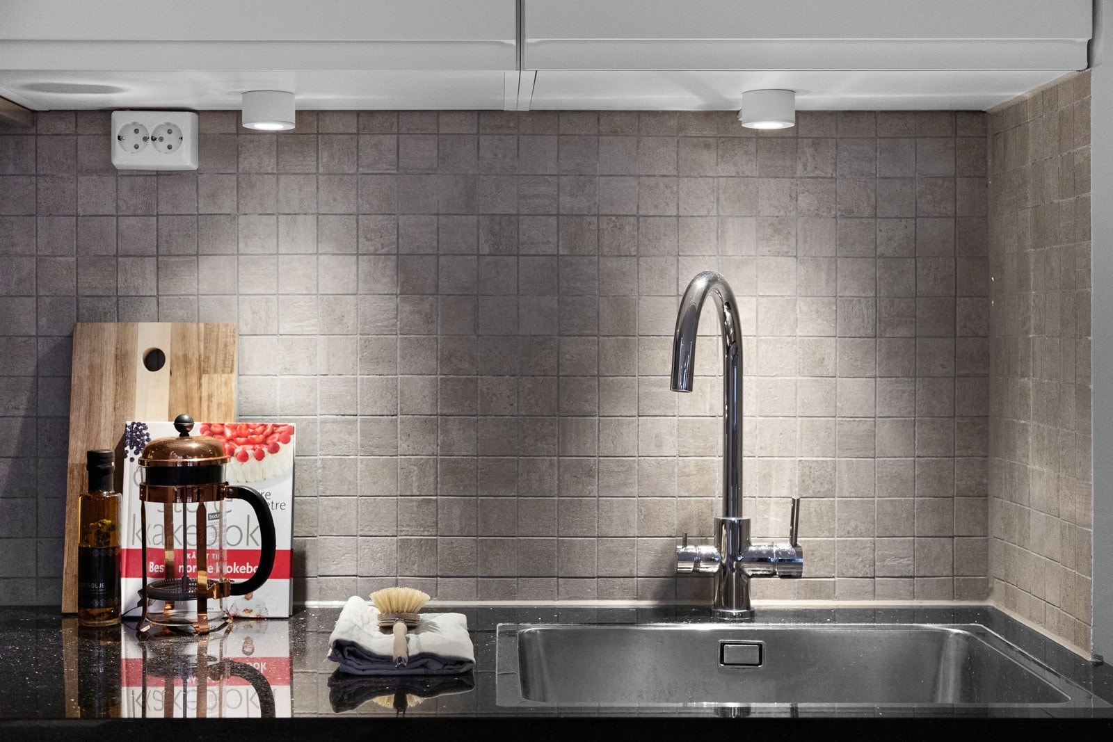 Dekorativt flisfelt mellom benkeskap og overskap samt montert belysning. Galleribilde